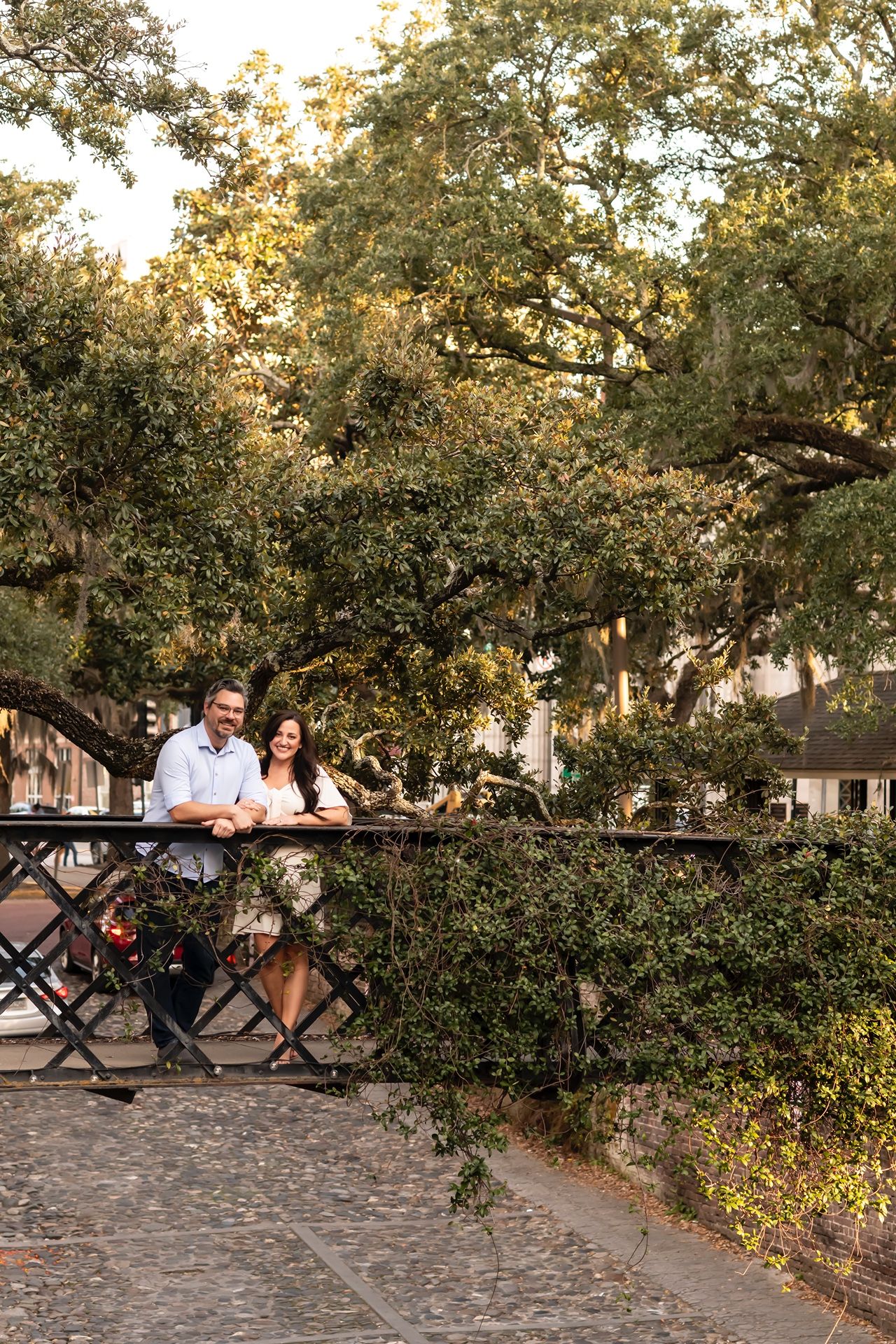 Couple enjoys an intimate moment at outdoor cafe seating surrounded by lush trees and greenery at sunset.