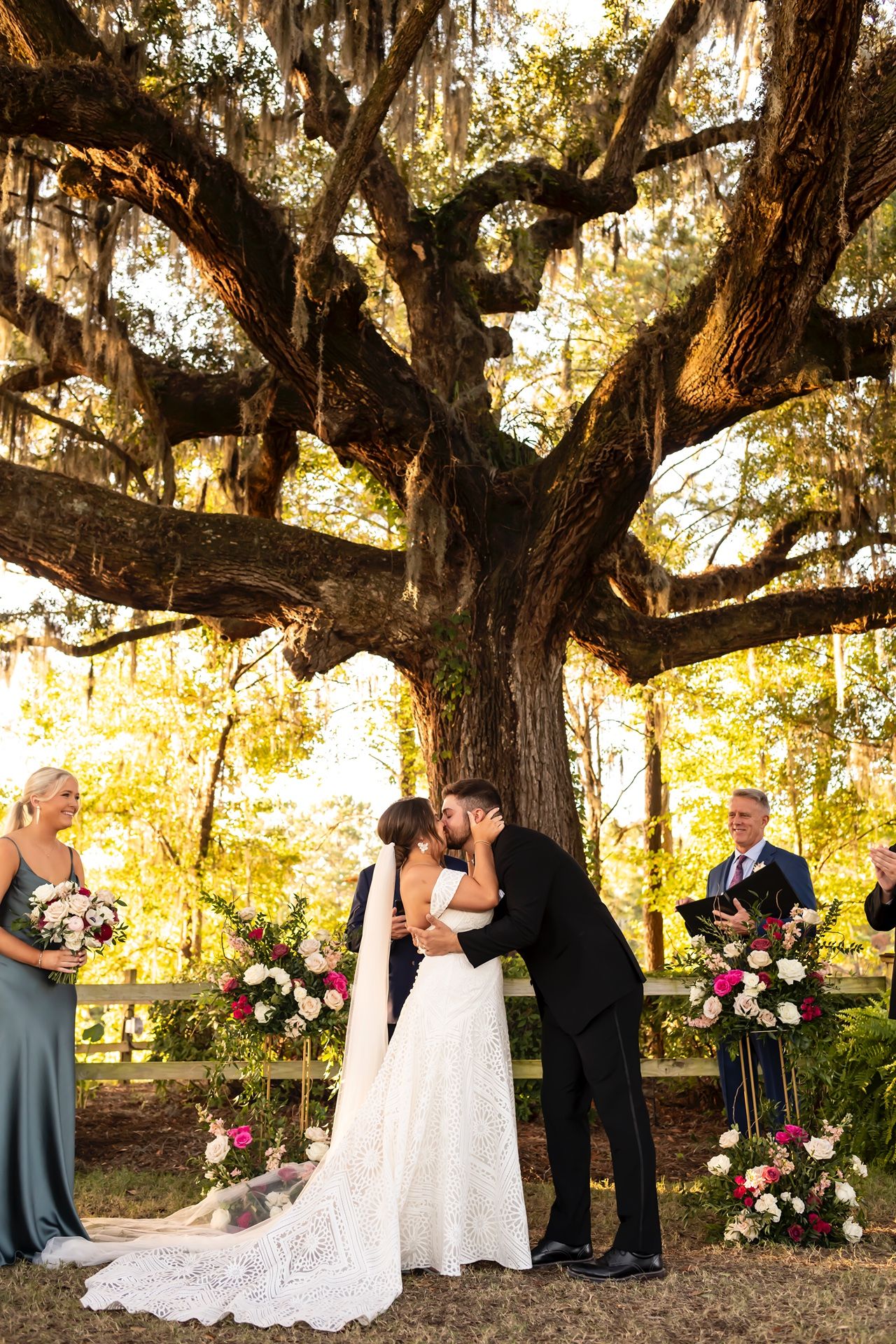 A romantic wedding ceremony takes place under a majestic oak tree draped with Spanish moss at golden hour.