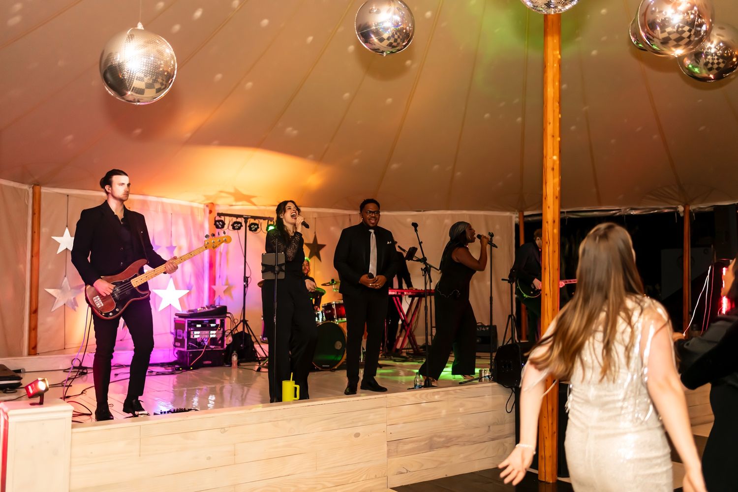 Wedding guests dancing under a disco ball and tent with colorful lighting during an evening reception celebration.