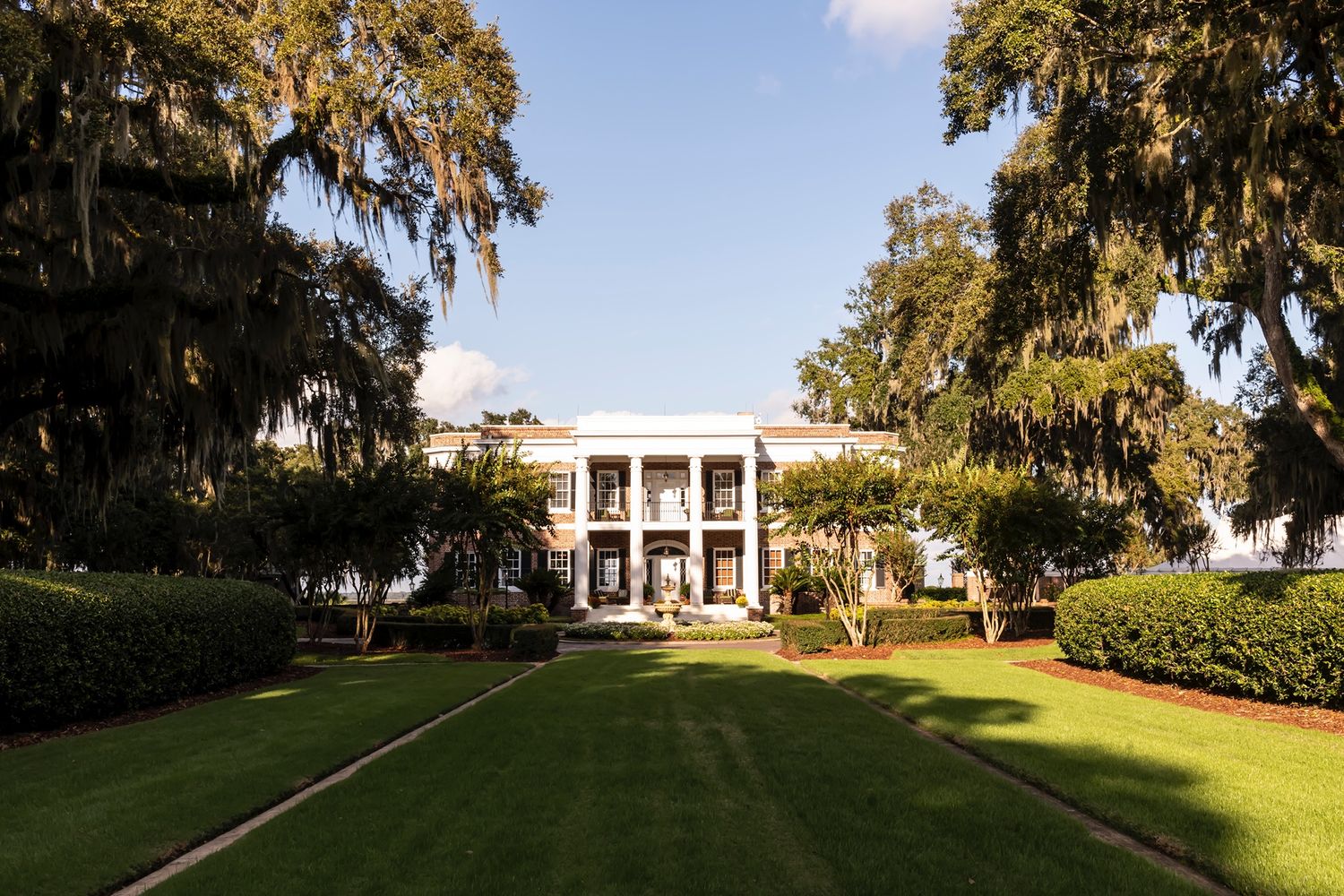 A grand antebellum mansion with white columns and Spanish moss-draped trees in the foreground.