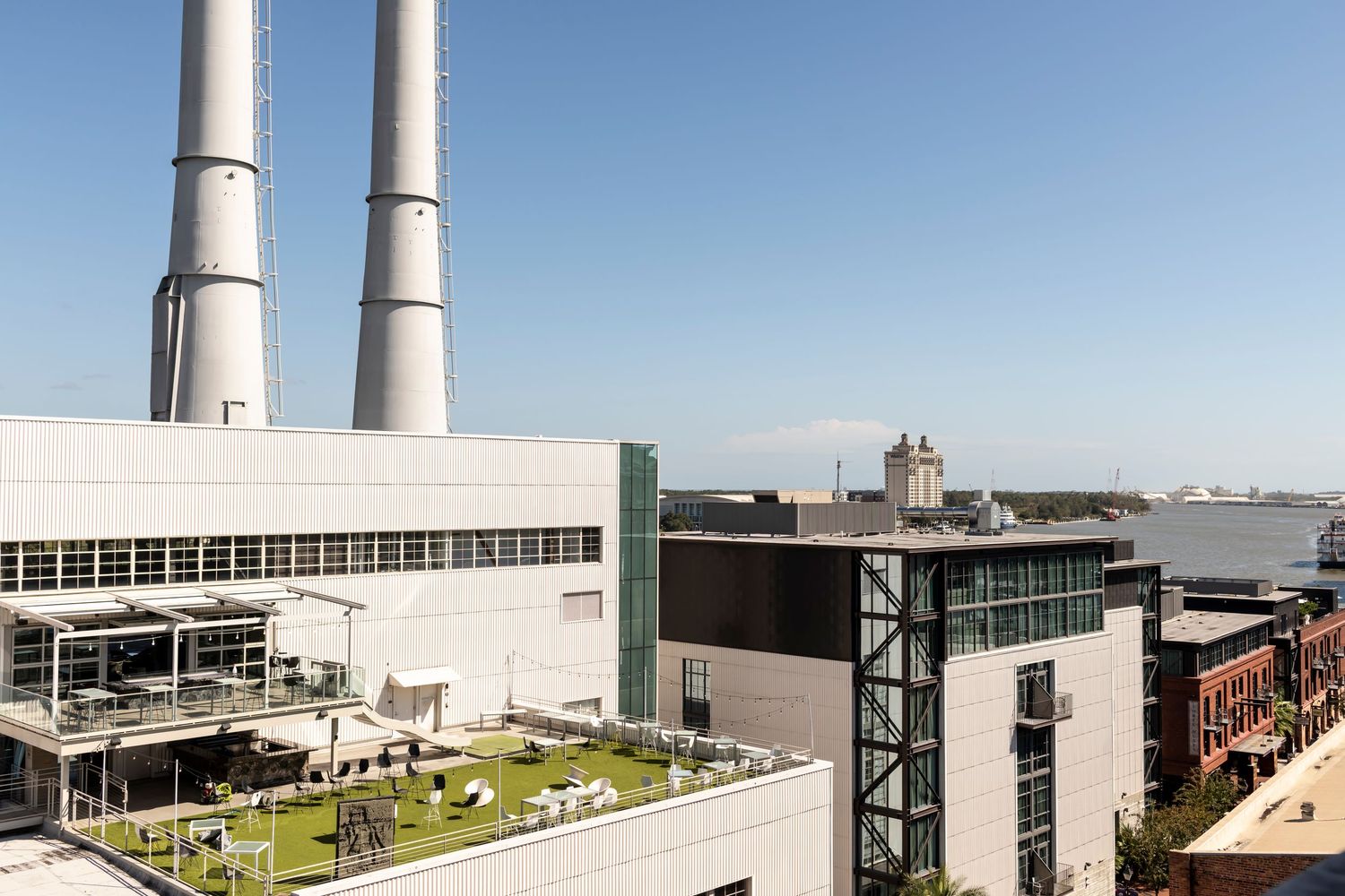 Industrial power plant with twin smokestacks against blue sky with modern buildings and waterfront view.