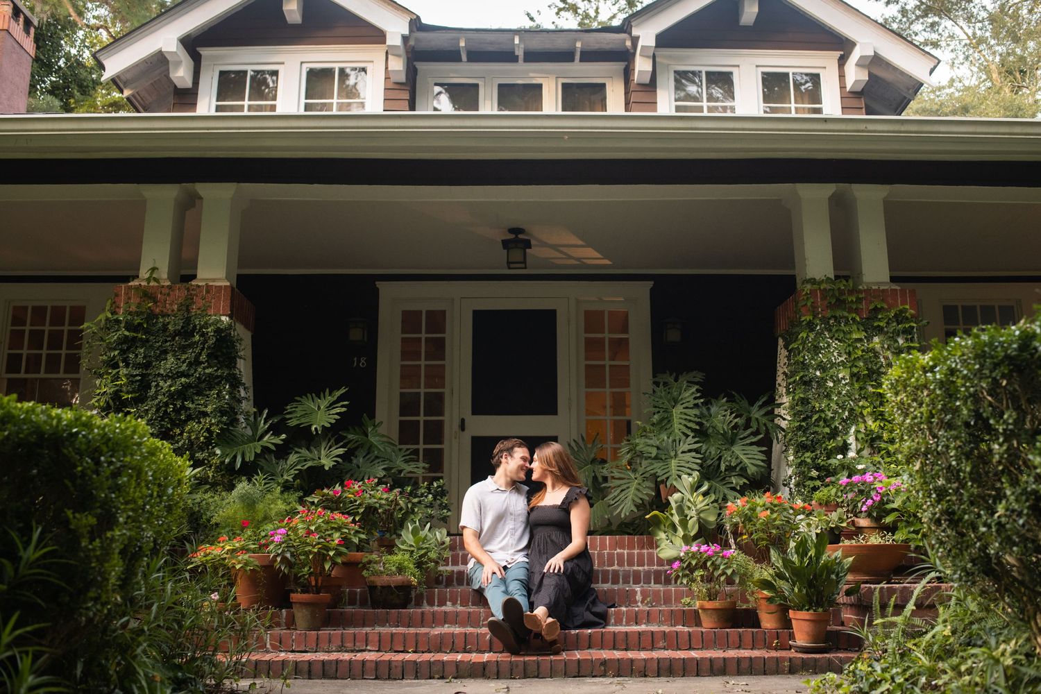 An engagement photoshoot on the front porch of a traditional home with white columns.
