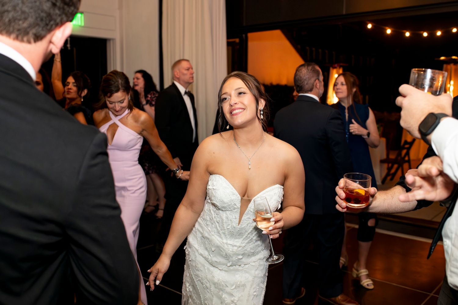 Wedding party members dance and socialize at an elegant indoor reception with warm lighting.