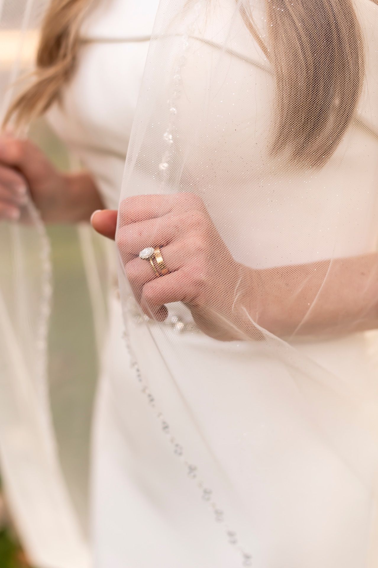 Close up of hands holding delicate white veil with sparkly details, showing engagement ring on wedding day.