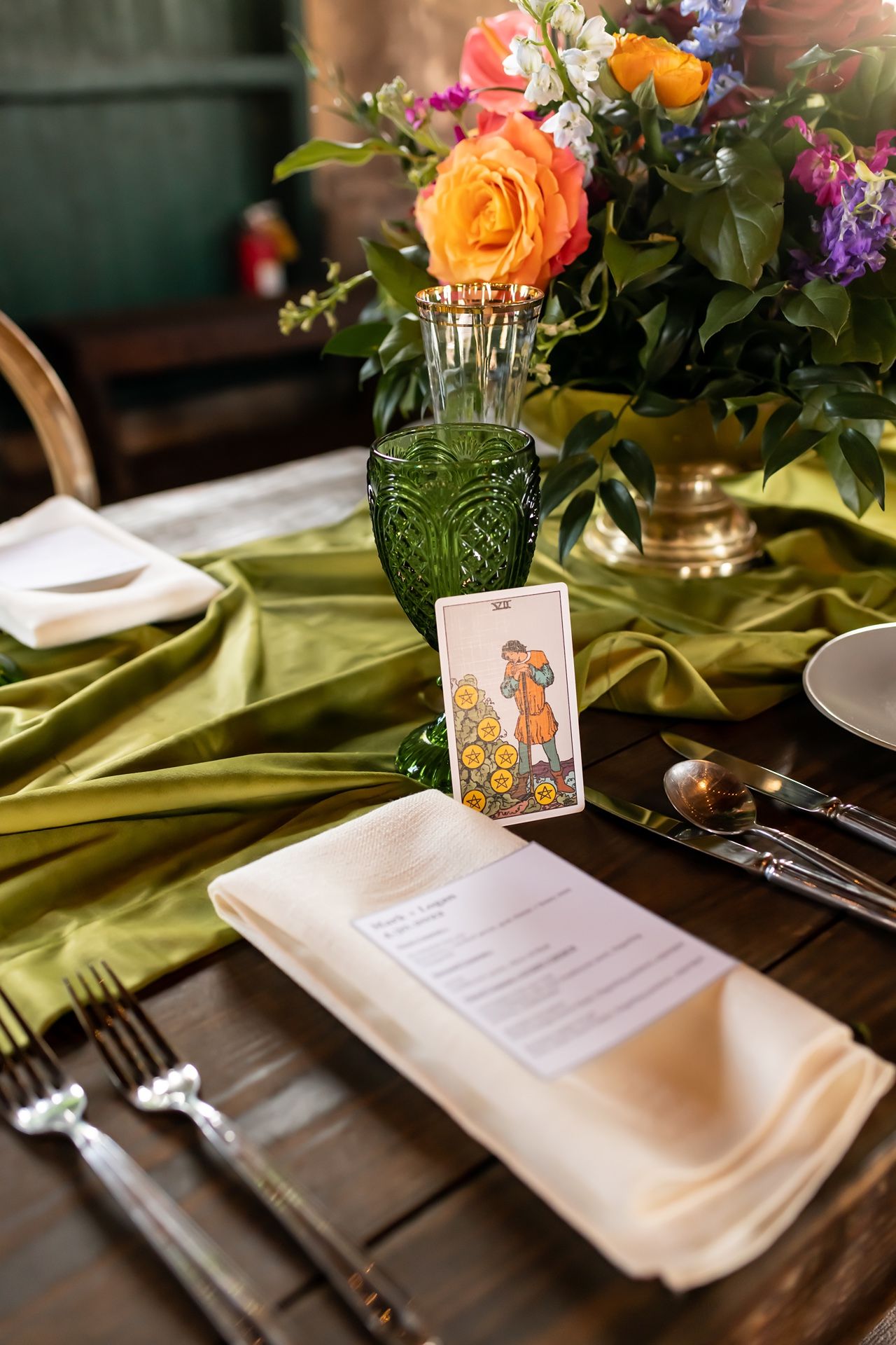 Table setting with green glassware, floral centerpiece, menu card and place card on olive green tablecloth.