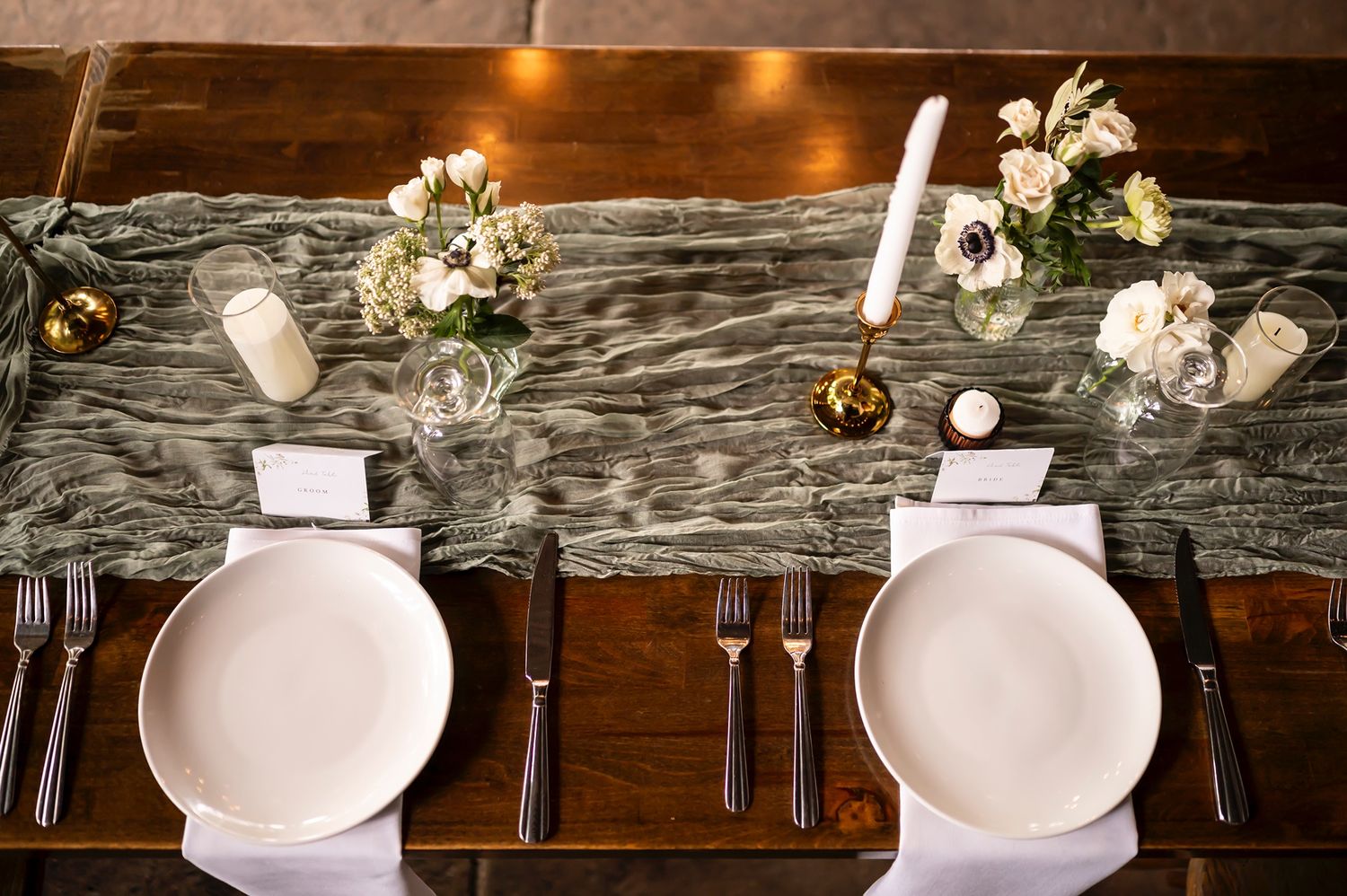 Elegant table setting with white plates, floral centerpieces and candles on marble-patterned runner at fine dining restaurant.