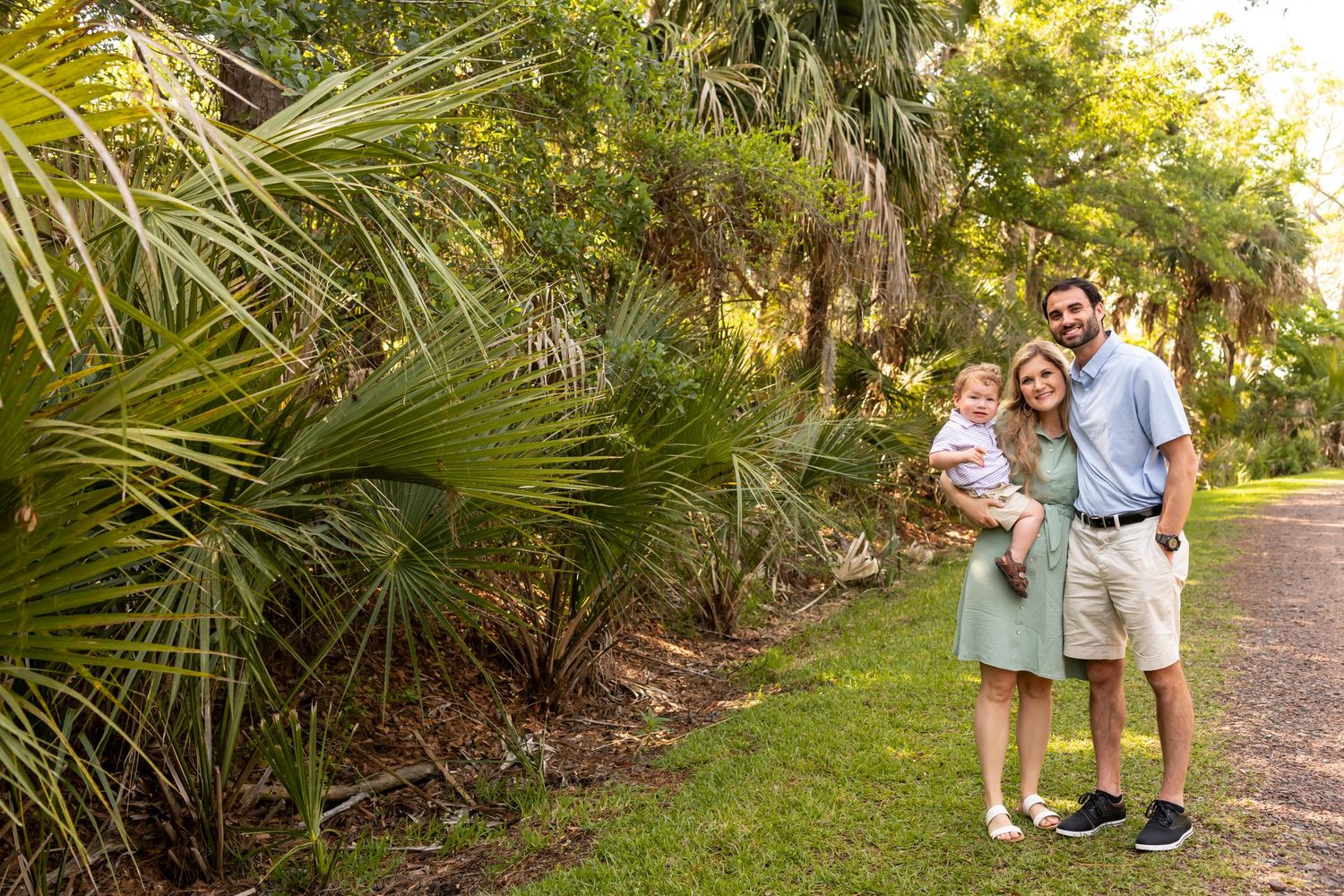 People standing on a path with lush palm trees and tropical foliage in a sunny garden setting.