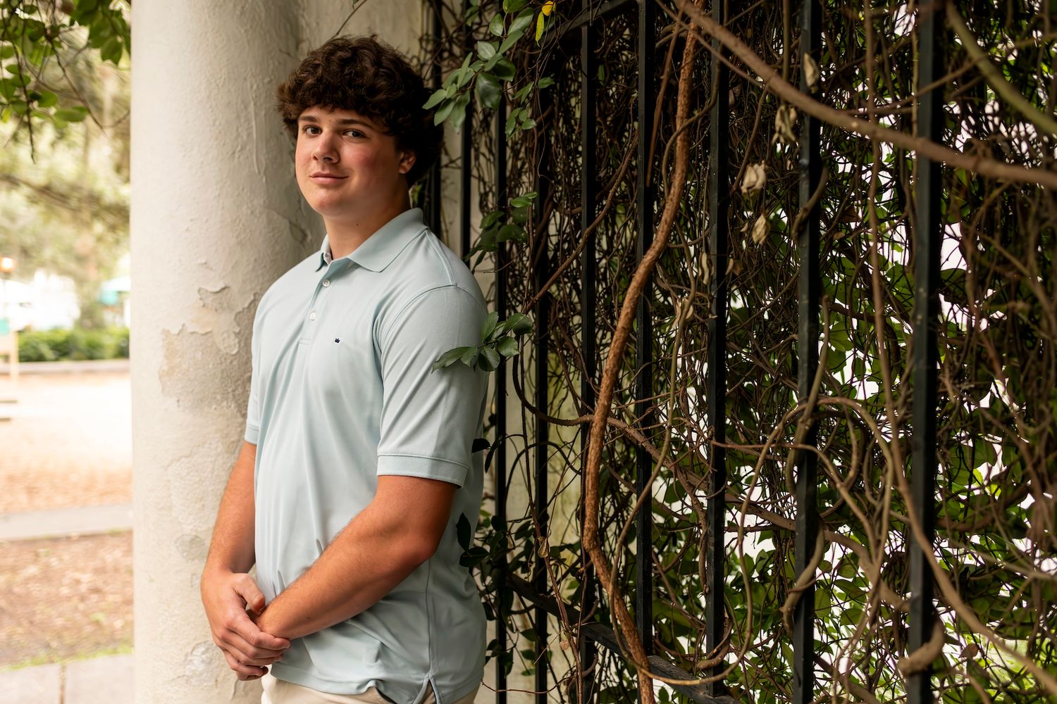 Portrait of person in light polo shirt leaning against column with climbing vines.