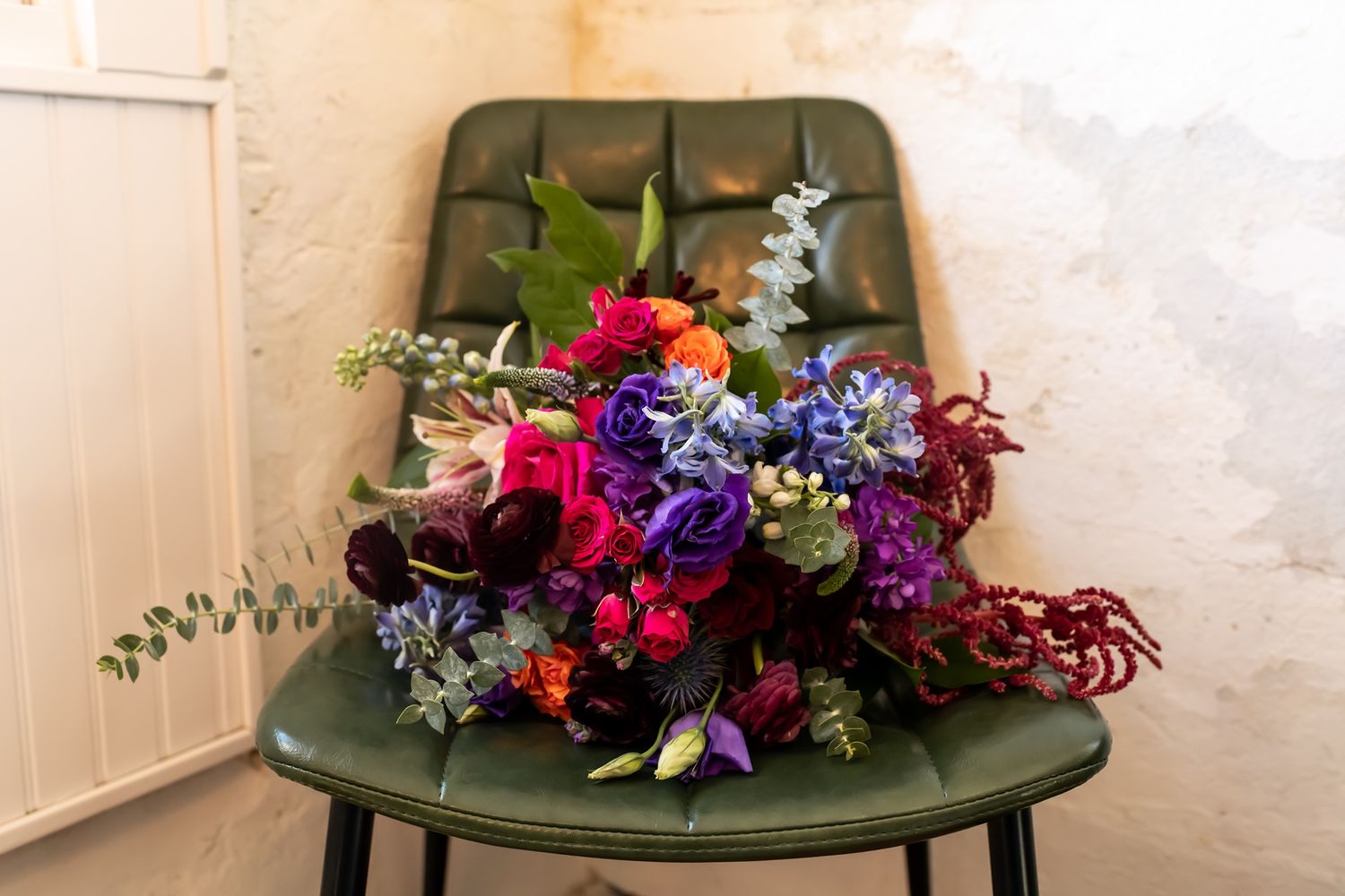 A vibrant floral arrangement with red, purple, and blue flowers sits on a vintage olive green chair.