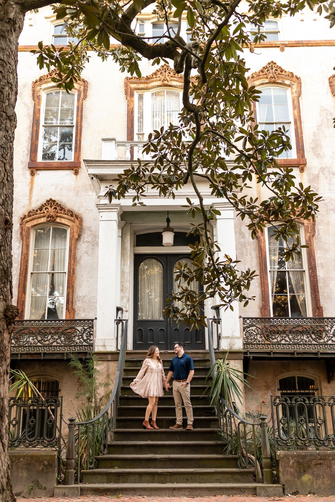Three historic row houses with ornate iron railings and stairs against a pink-tinged wall along a tree-lined street.