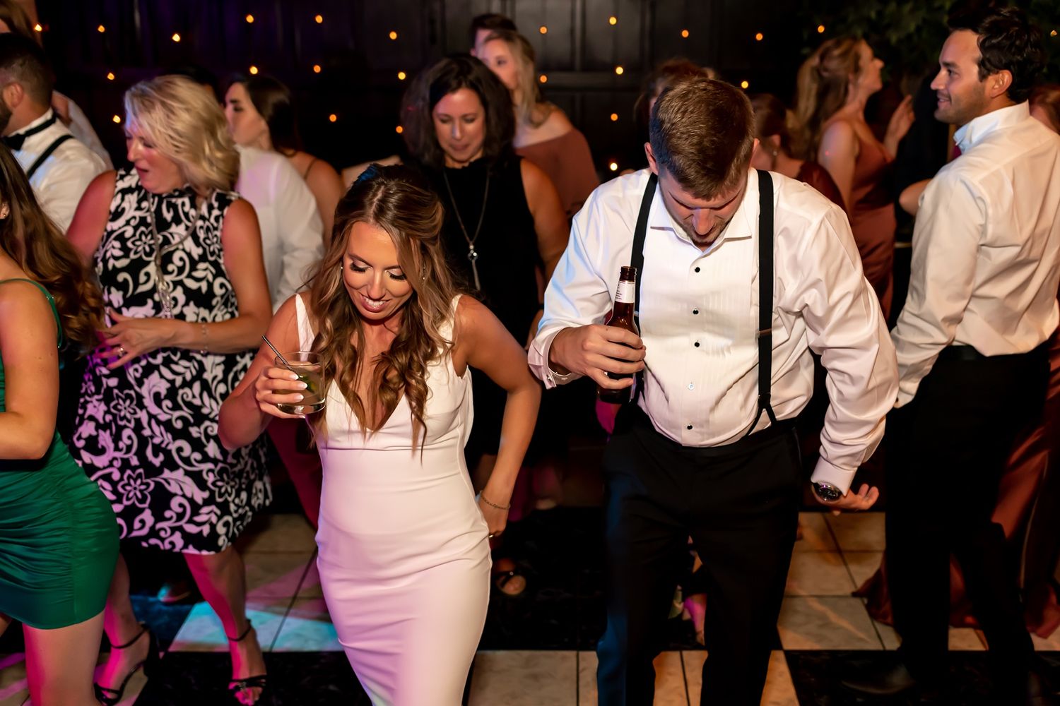 Wedding guests dance together in a dimly lit reception hall with festive party lighting.