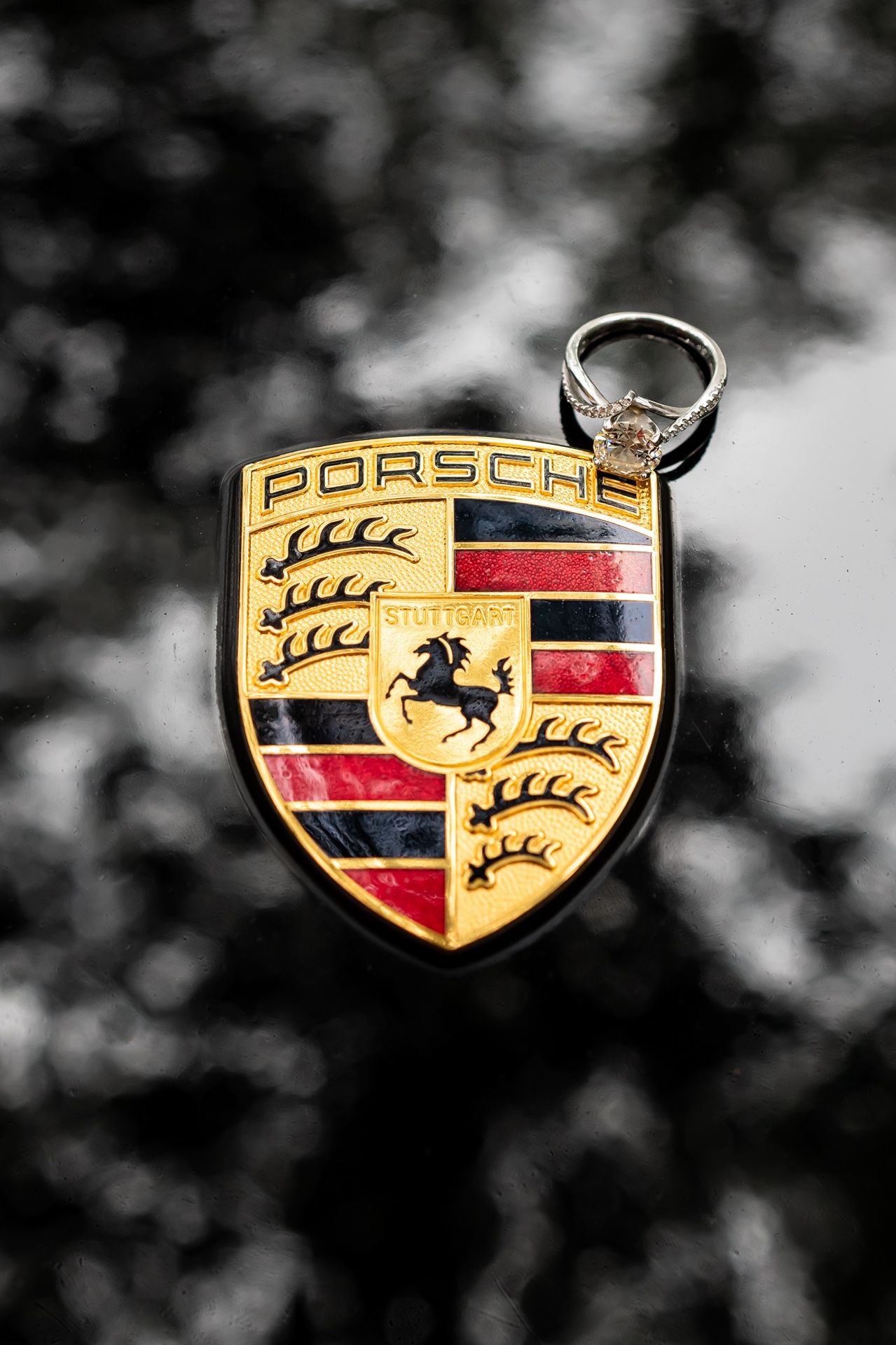 Close-up of a gold and red Porsche car emblem keychain against a blurred dark background.