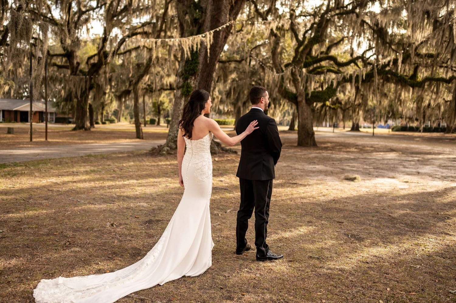 A wedding couple strolls together beneath the hanging Spanish moss at a southern plantation venue during golden hour.