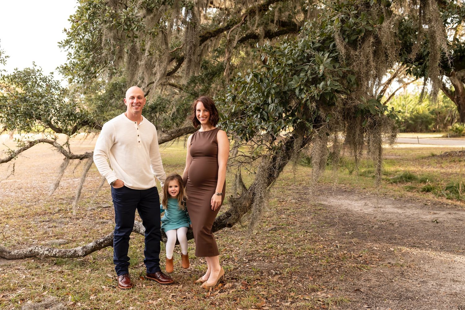 A multigenerational family enjoys time together outdoors under Spanish moss hanging from trees at sunset.