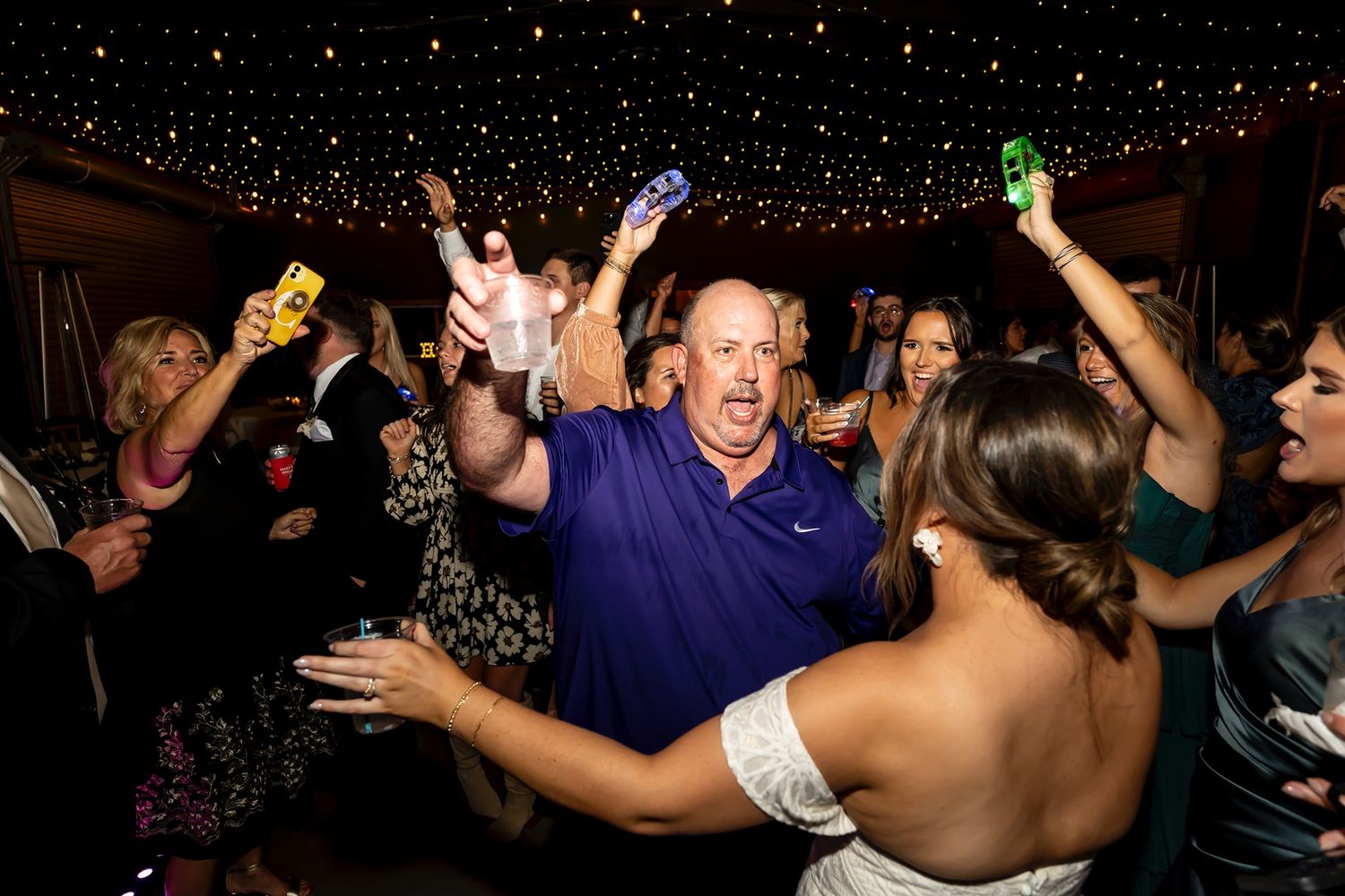 Excited crowd of party-goers dancing and celebrating under twinkling lights at a nightclub event.