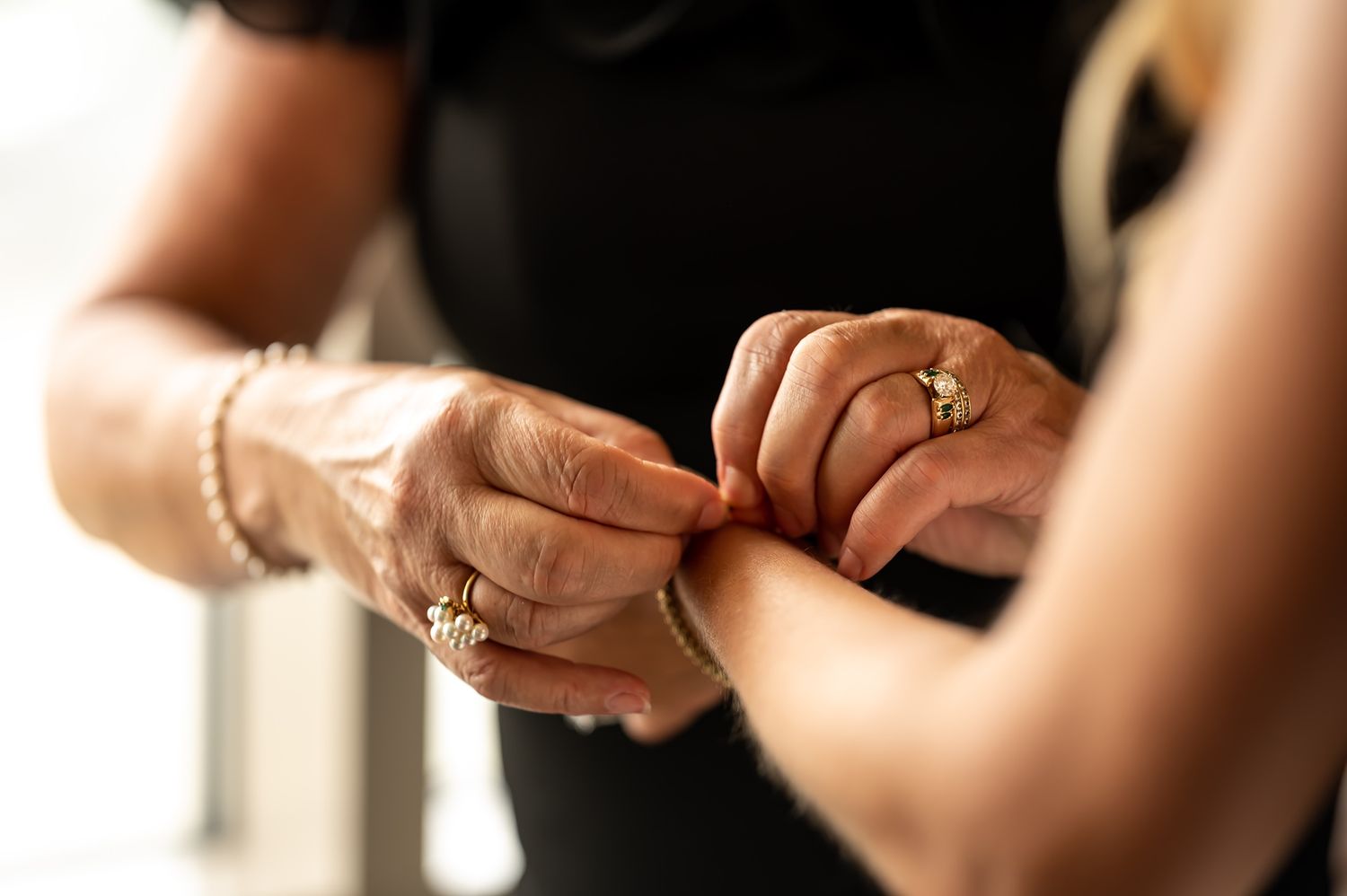 Two hands perform the delicate art of bead stringing using brown beaded cords and silver findings.
