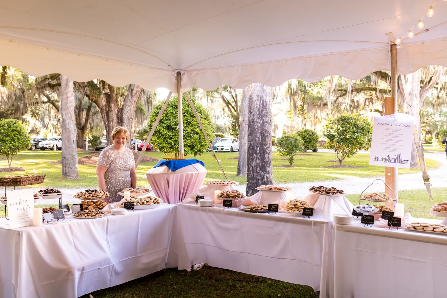 A wedding reception setup under an outdoor tent with white tablecloths and string lights for decoration.