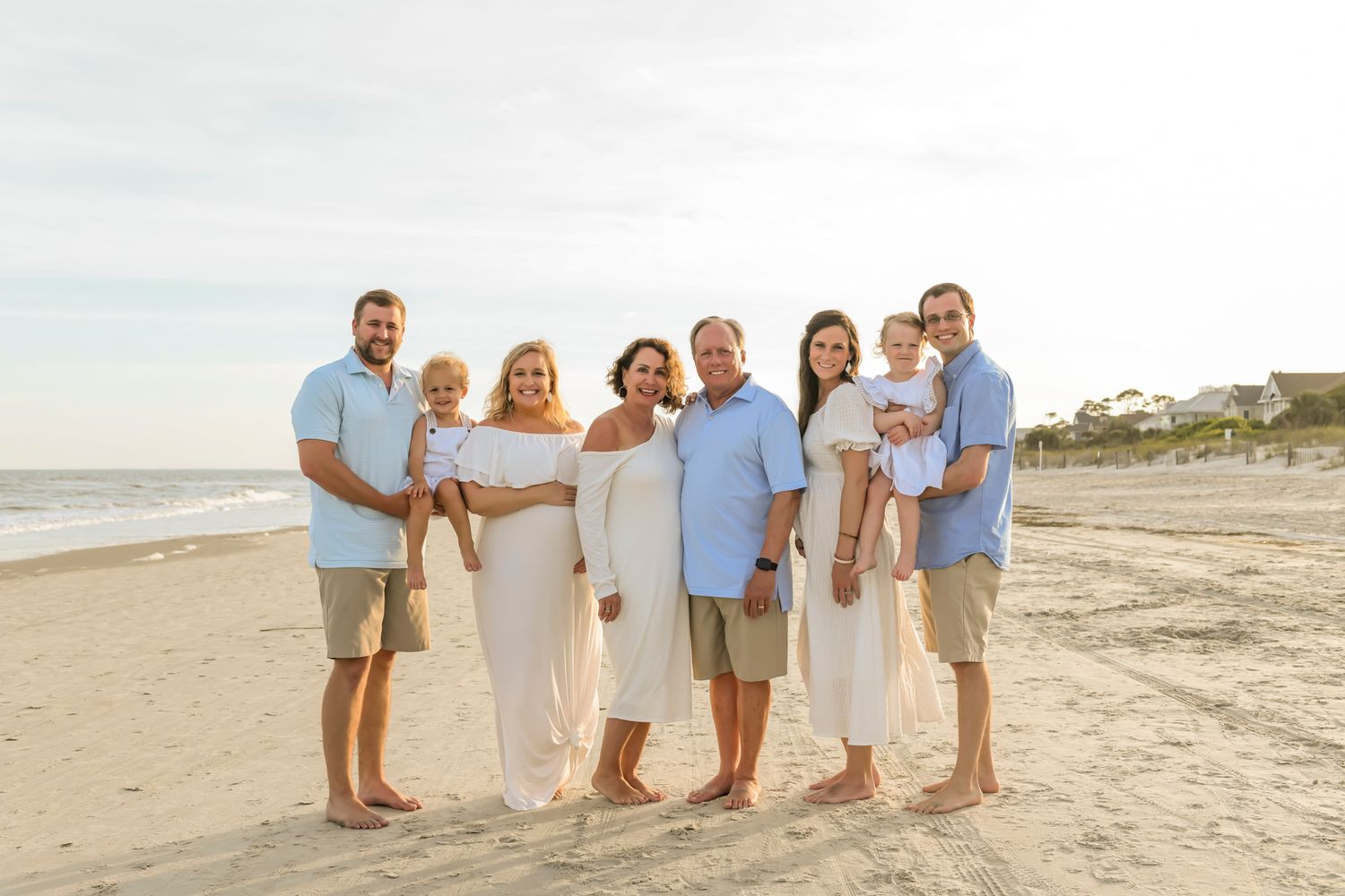 A family group stands together on a sunny beach at sunset wearing coordinated white and blue coastal attire.