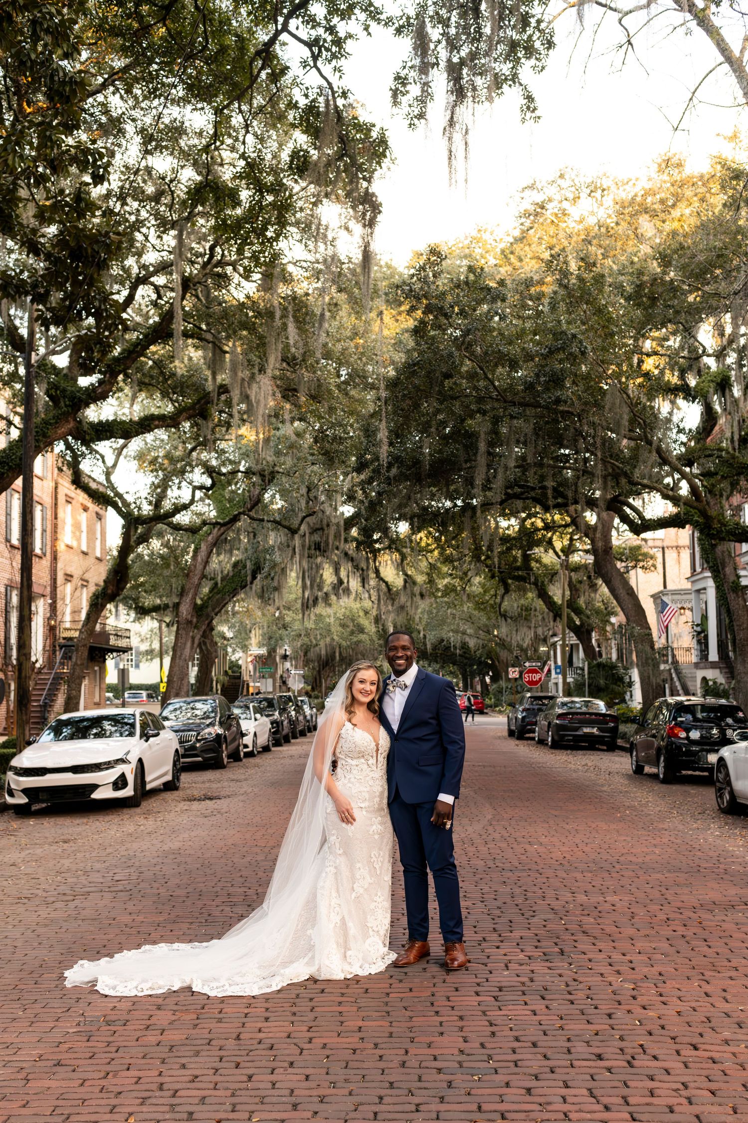 Wedding couple poses on historic brick street lined with Spanish moss-draped oak trees in Savannah's downtown district.