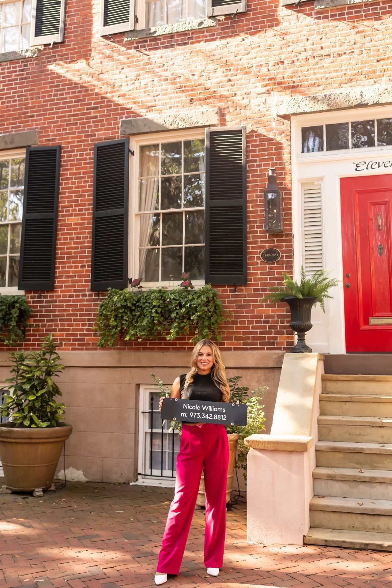 A brick townhouse with black shutters, a red door, and flower boxes on a charming city street in autumn.