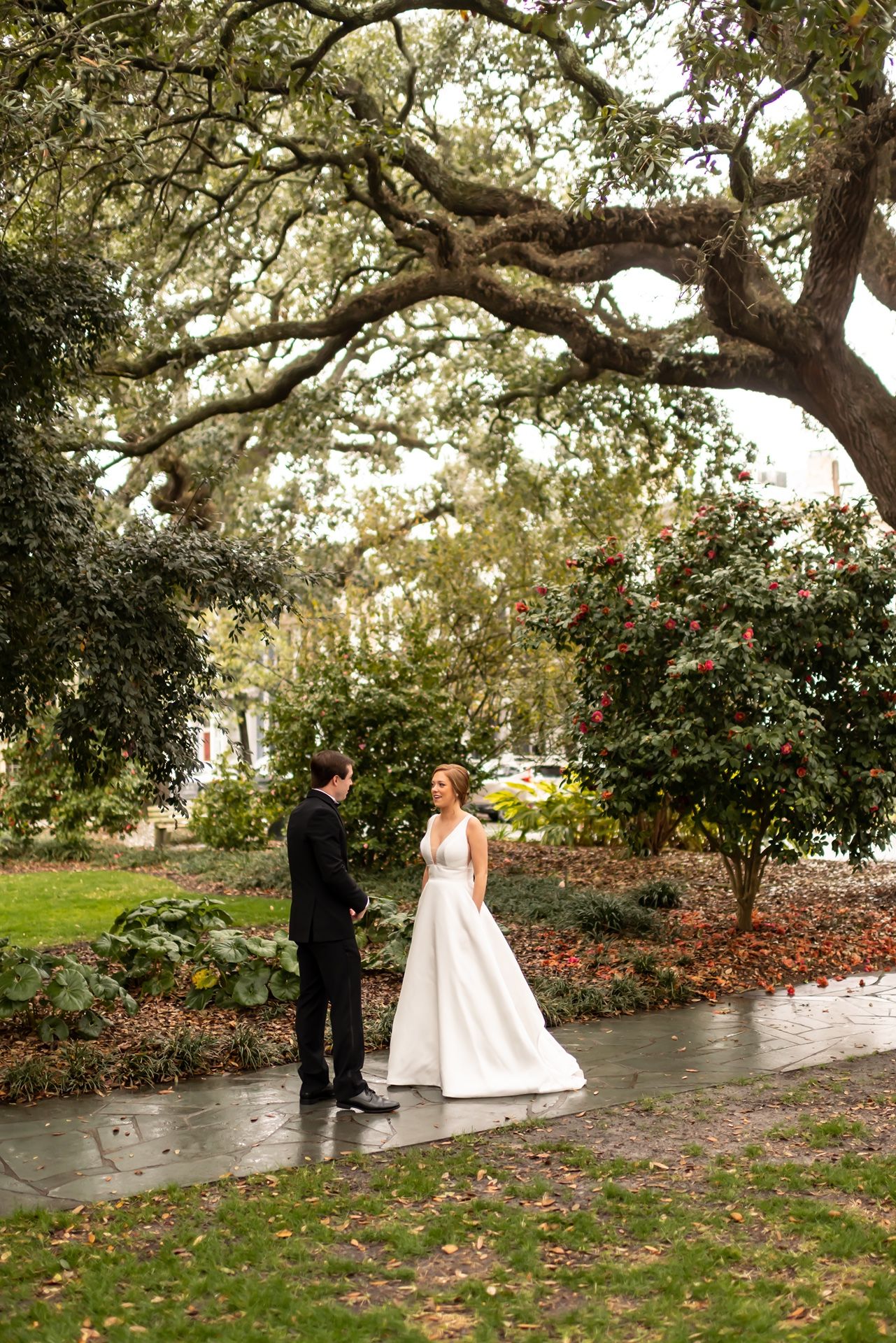 A couple stands beneath a majestic oak tree in a garden setting during an autumn wedding ceremony.
