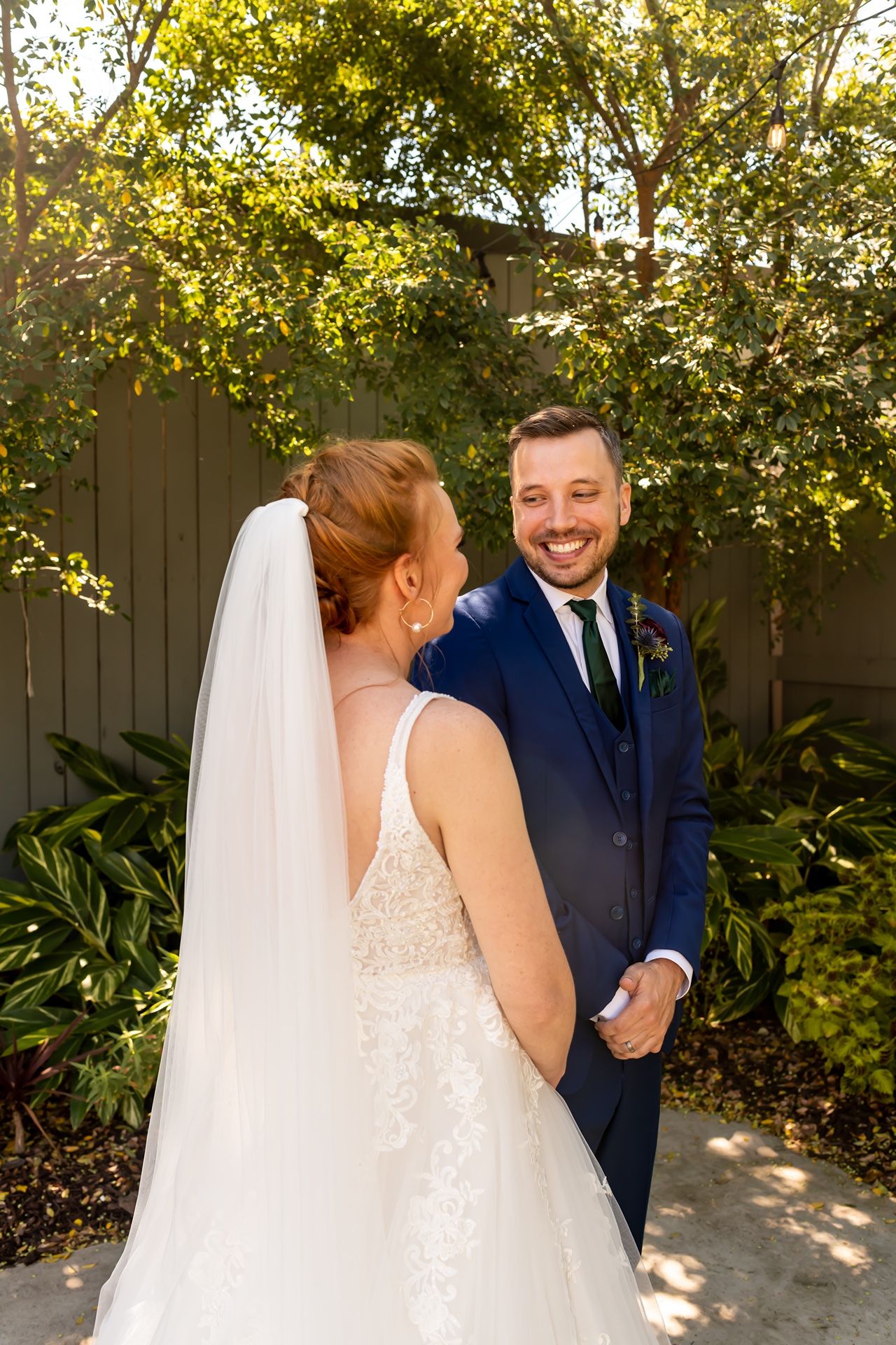 Couple on their wedding day shows emotional reactions during a first look in an outdoor garden setting with tall trees.