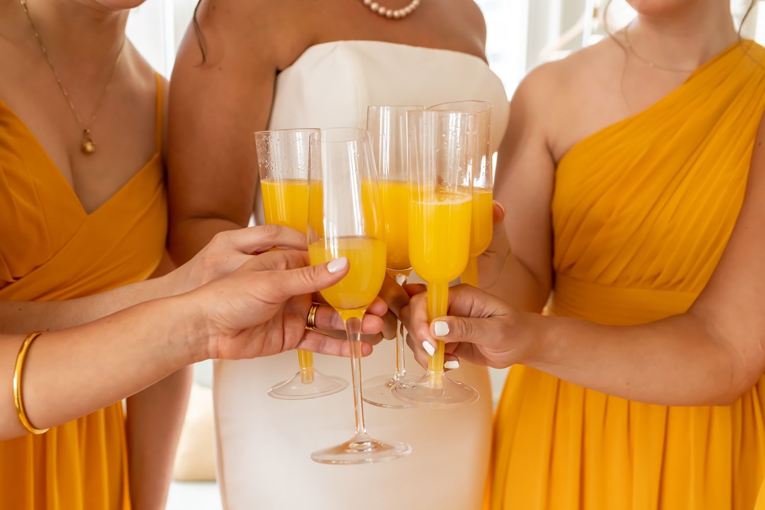 A row of bridesmaids in bright yellow dresses hold champagne glasses during a wedding celebration.