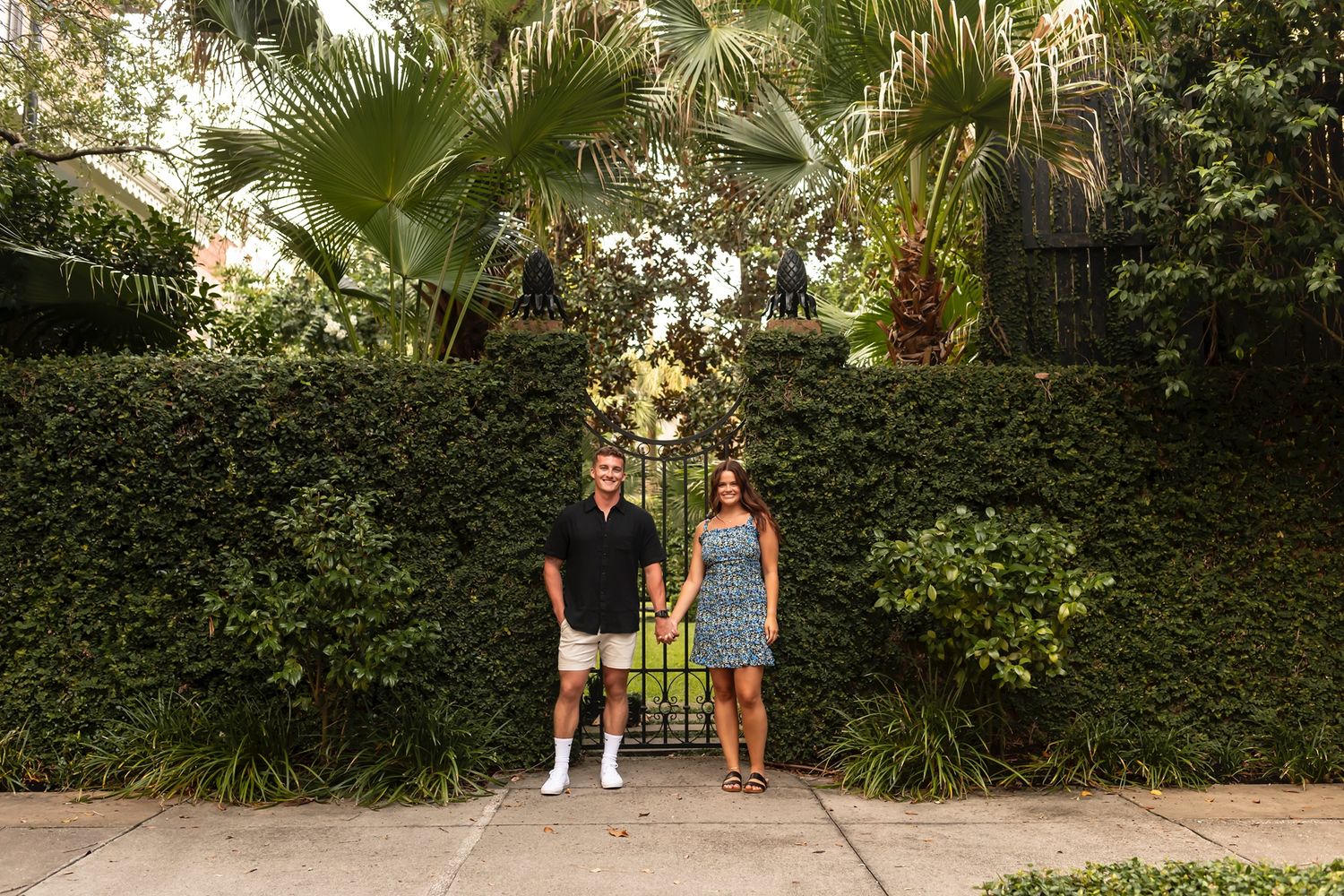 A couple takes an afternoon stroll along a lush garden pathway surrounded by tropical plants and greenery.