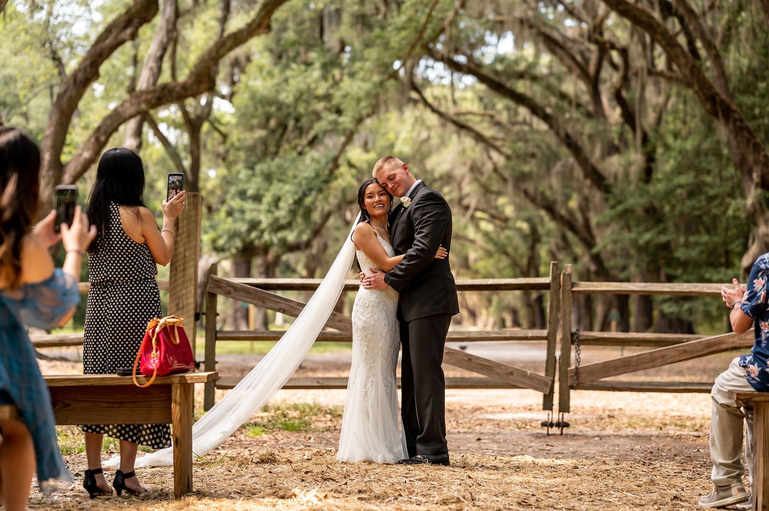 A couple shares an intimate moment beneath Spanish moss-covered trees on a wooden walkway at their outdoor ceremony.