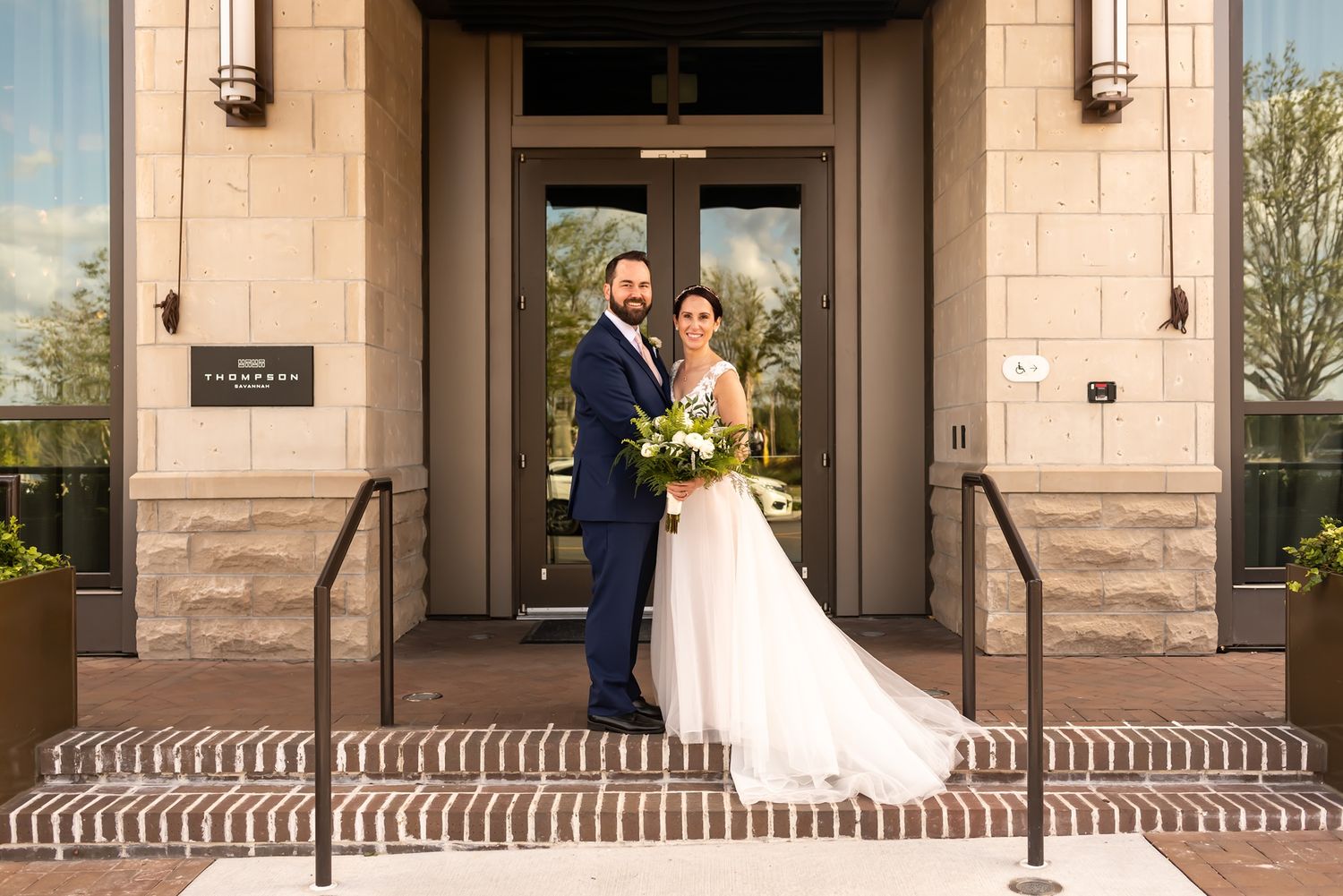 A couple poses for their wedding portrait in front of a grand building entrance with stone steps and columns.