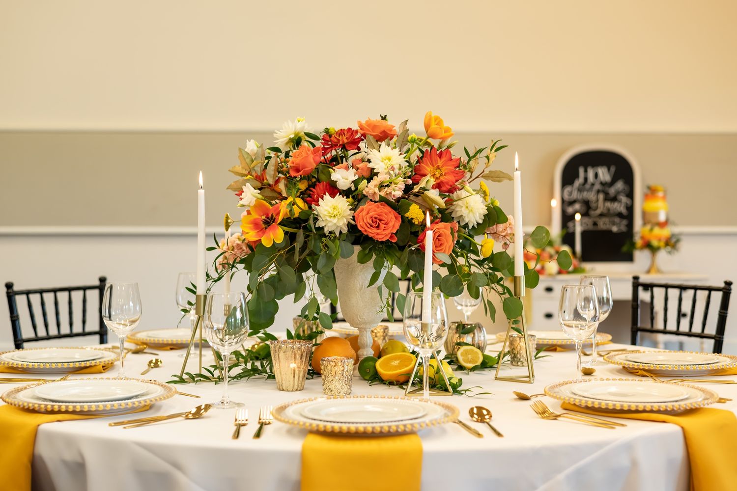 Orange and pink floral centerpieces adorn an elegant table setting with golden accents and black chiavari chairs.