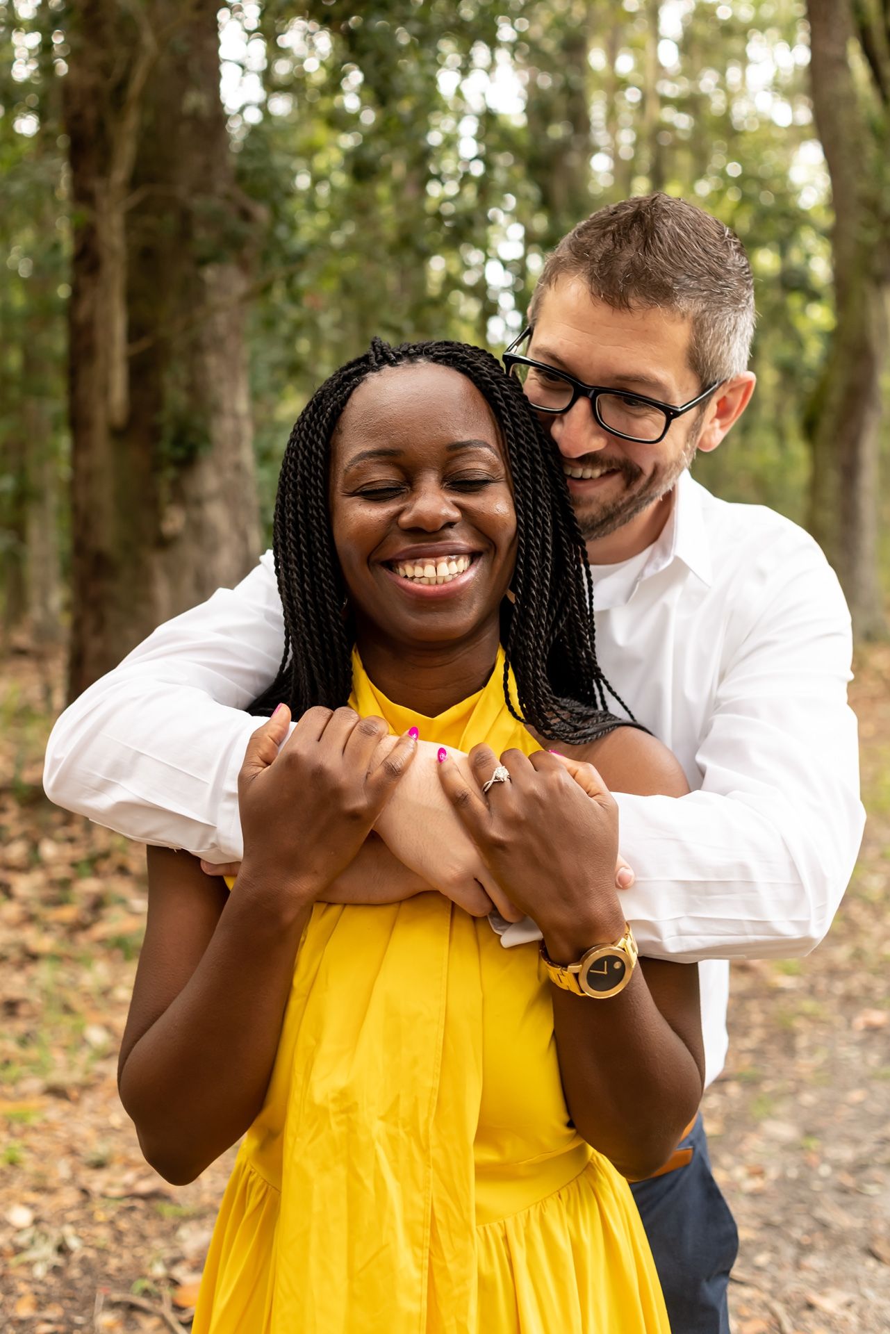 A couple shares a joyful candid moment together outdoors surrounded by trees in a romantic photoshoot.