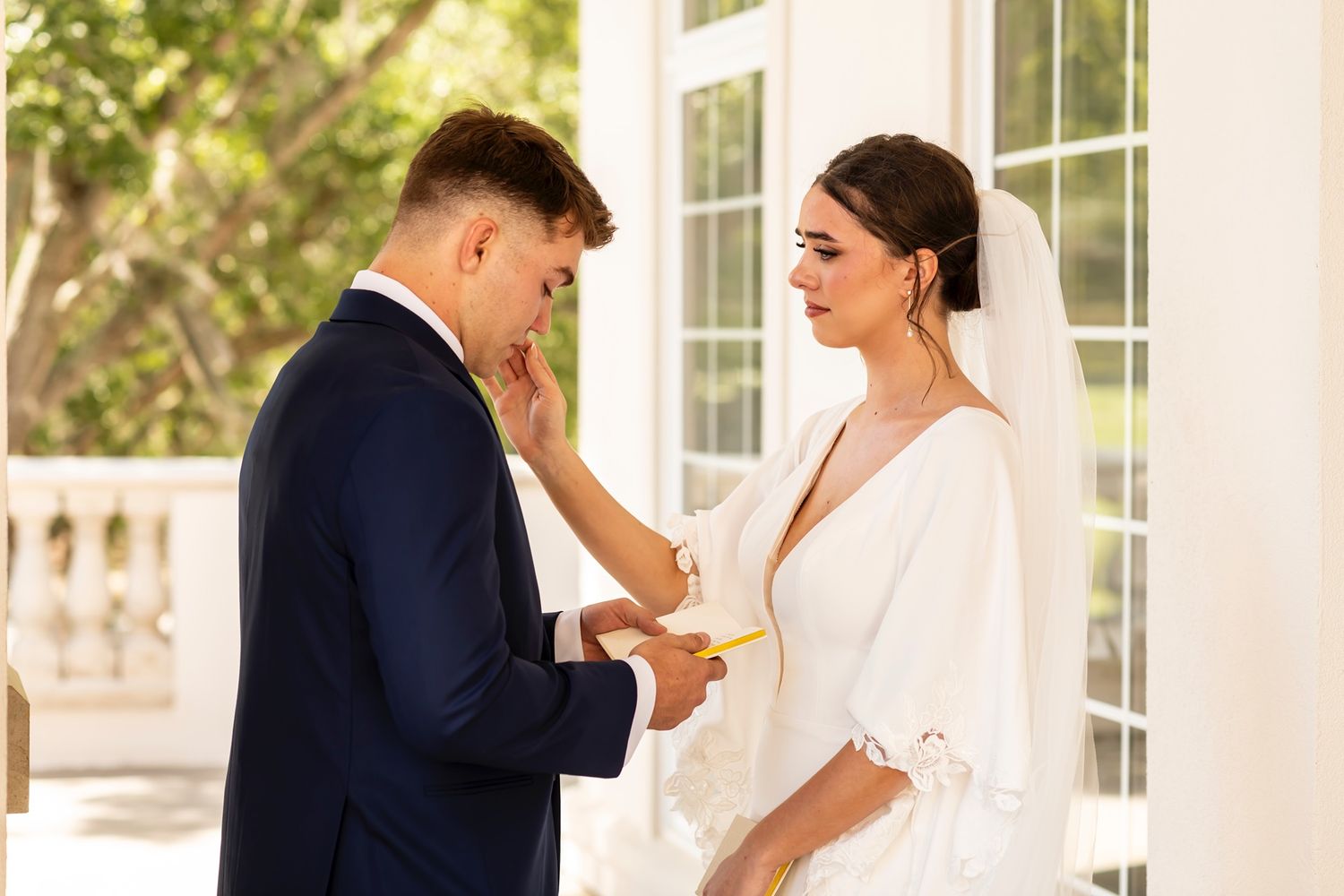 Bride and groom share a joyful moment dancing together on a sunlit porch during their wedding celebration.