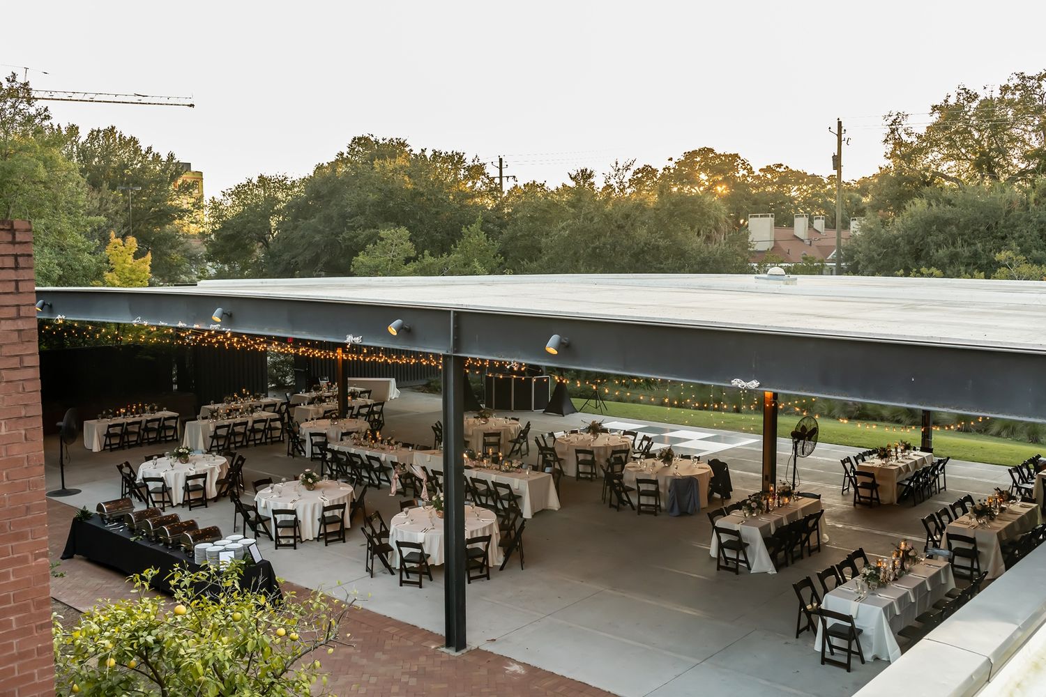 An outdoor covered patio dining area with tables and chairs arranged under a large canopy during golden hour.