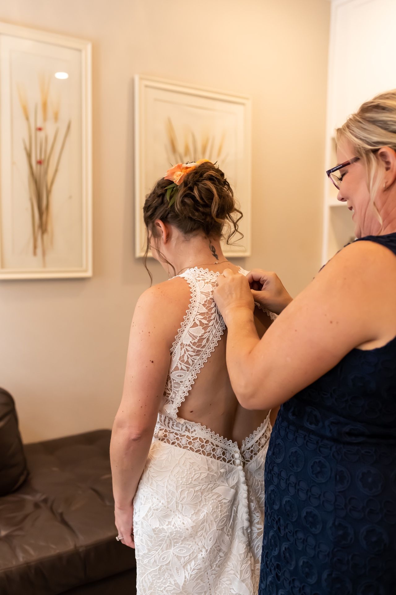 Someone helping to button up an elegant white lace wedding dress during bridal preparations.