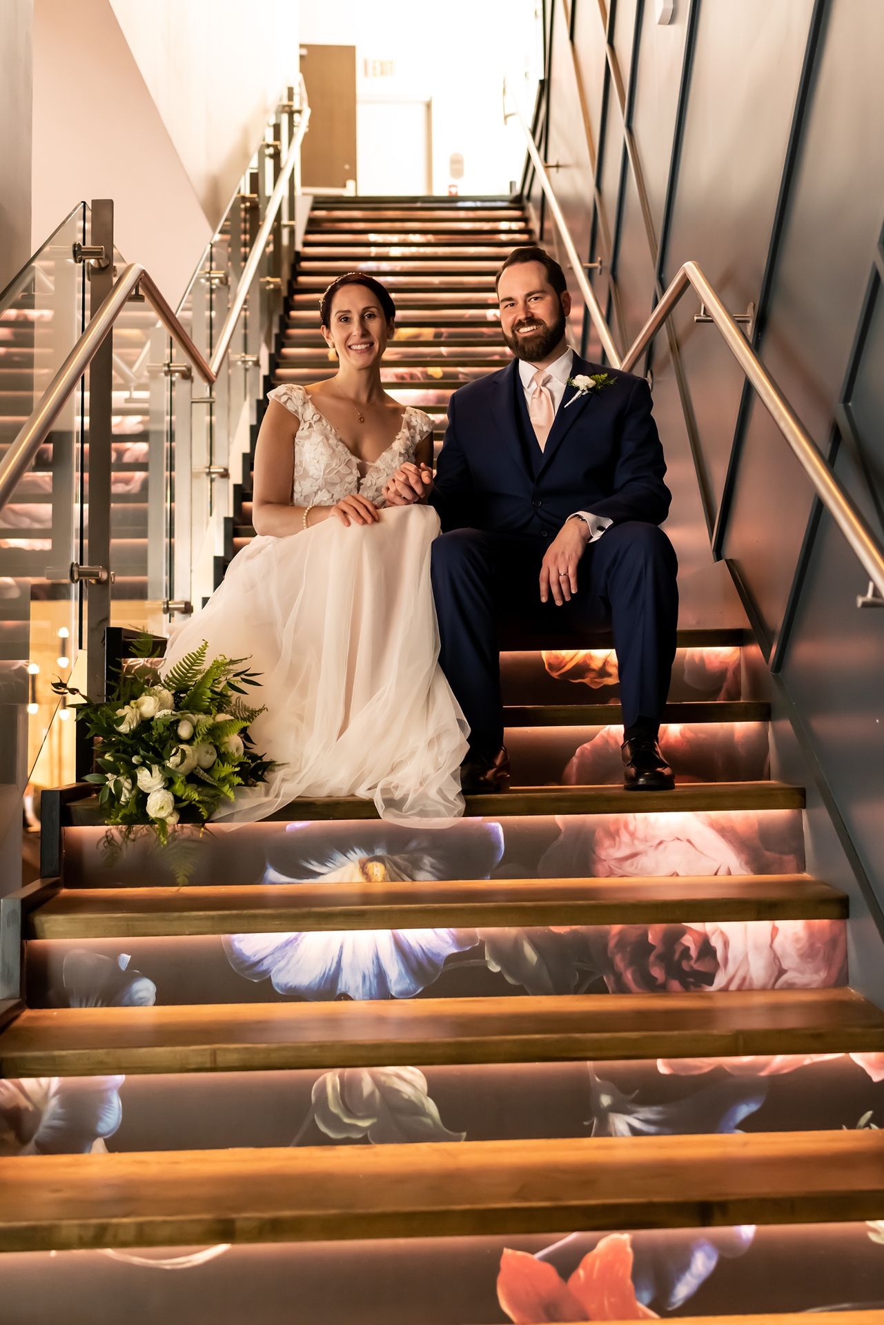 Bride and groom sit together on illuminated stairs decorated with floral projections at their wedding venue.