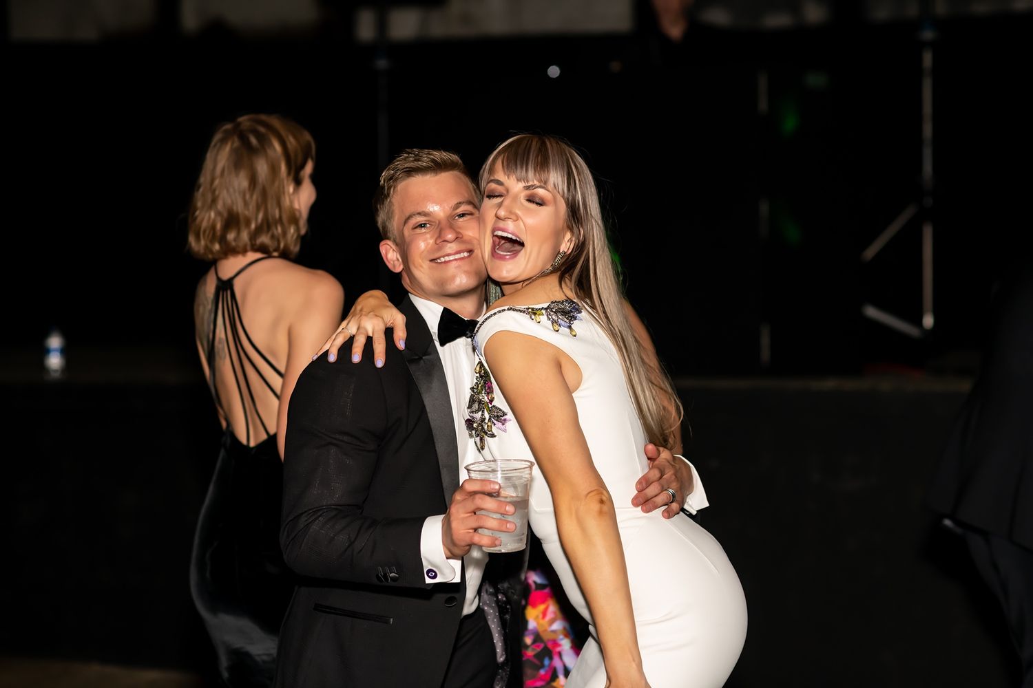 Two people embracing and smiling while dancing together at a darkly lit indoor event.
