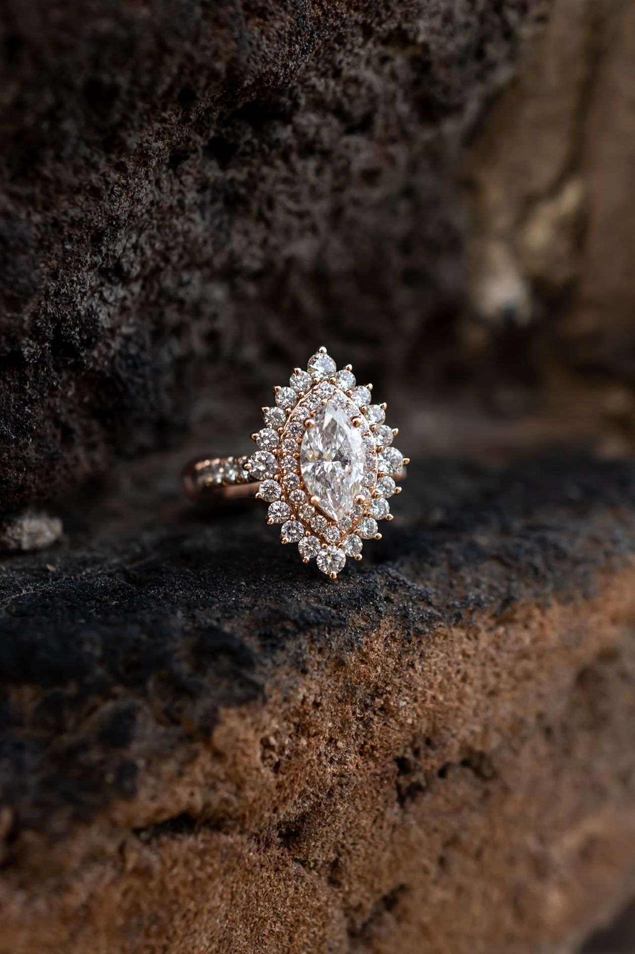 Stunning vintage-inspired marquise diamond engagement ring in rose gold setting rests on textured dark surface.