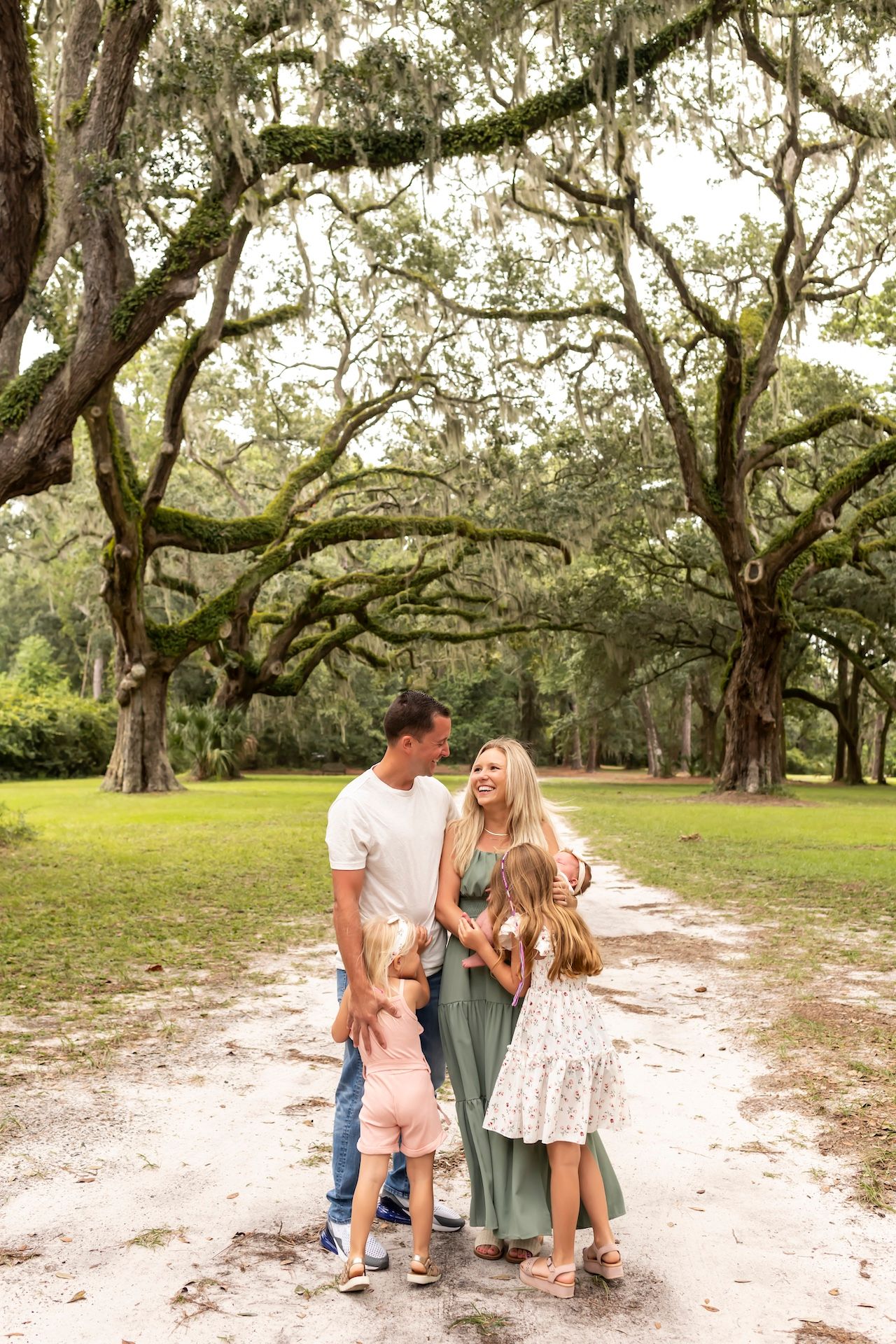 A family shares a tender moment together on a sandy path beneath sprawling oak trees in a natural outdoor setting.