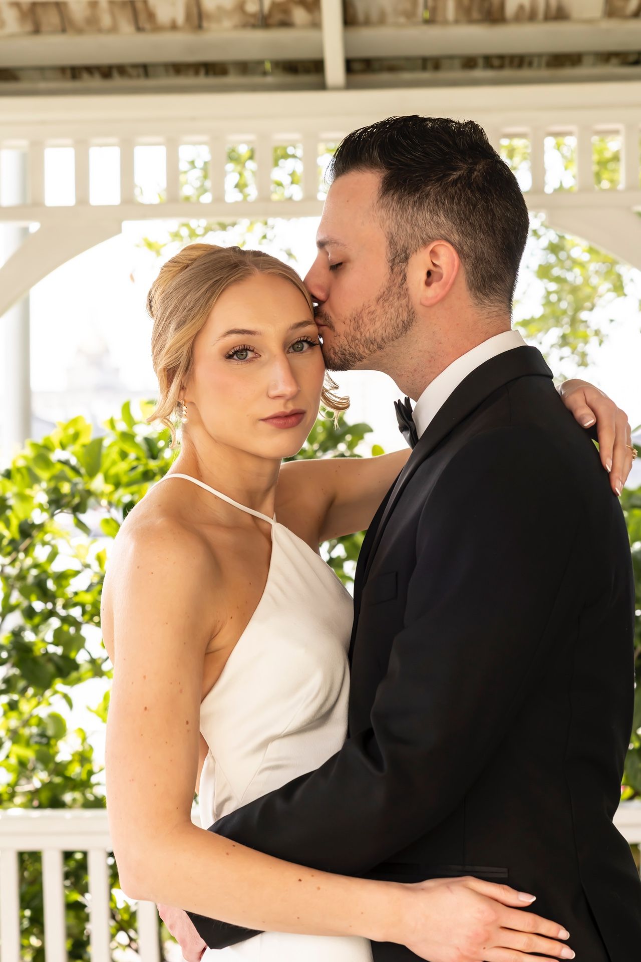 An intimate moment captured under a white gazebo surrounded by greenery.