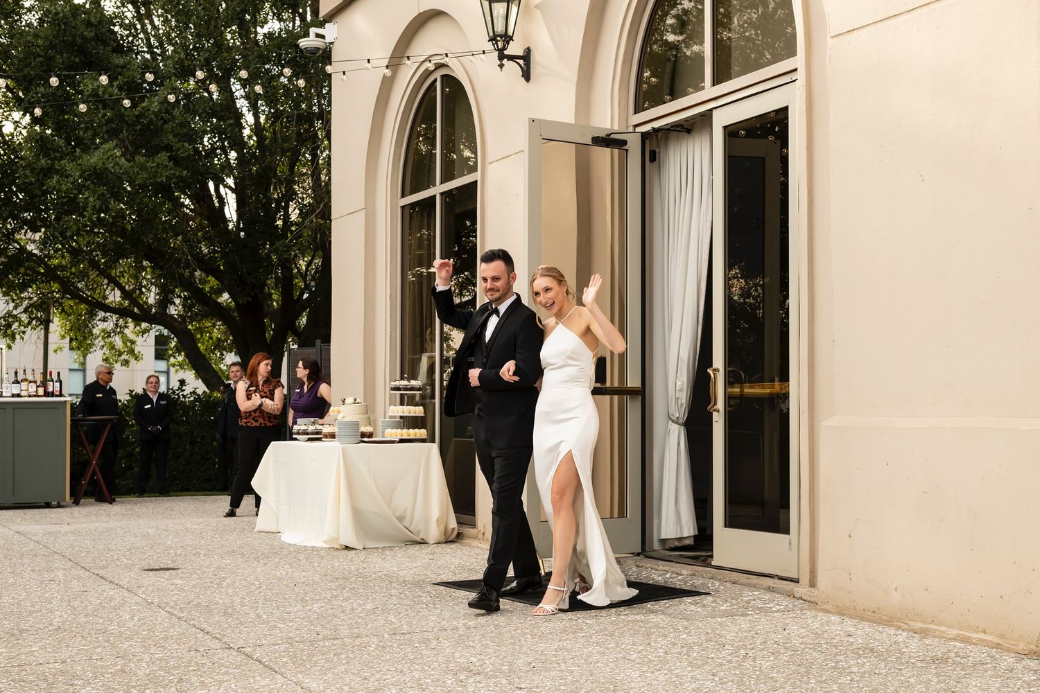 A couple in formal attire steps out through elegant arched doorway of a grand venue on their wedding day.