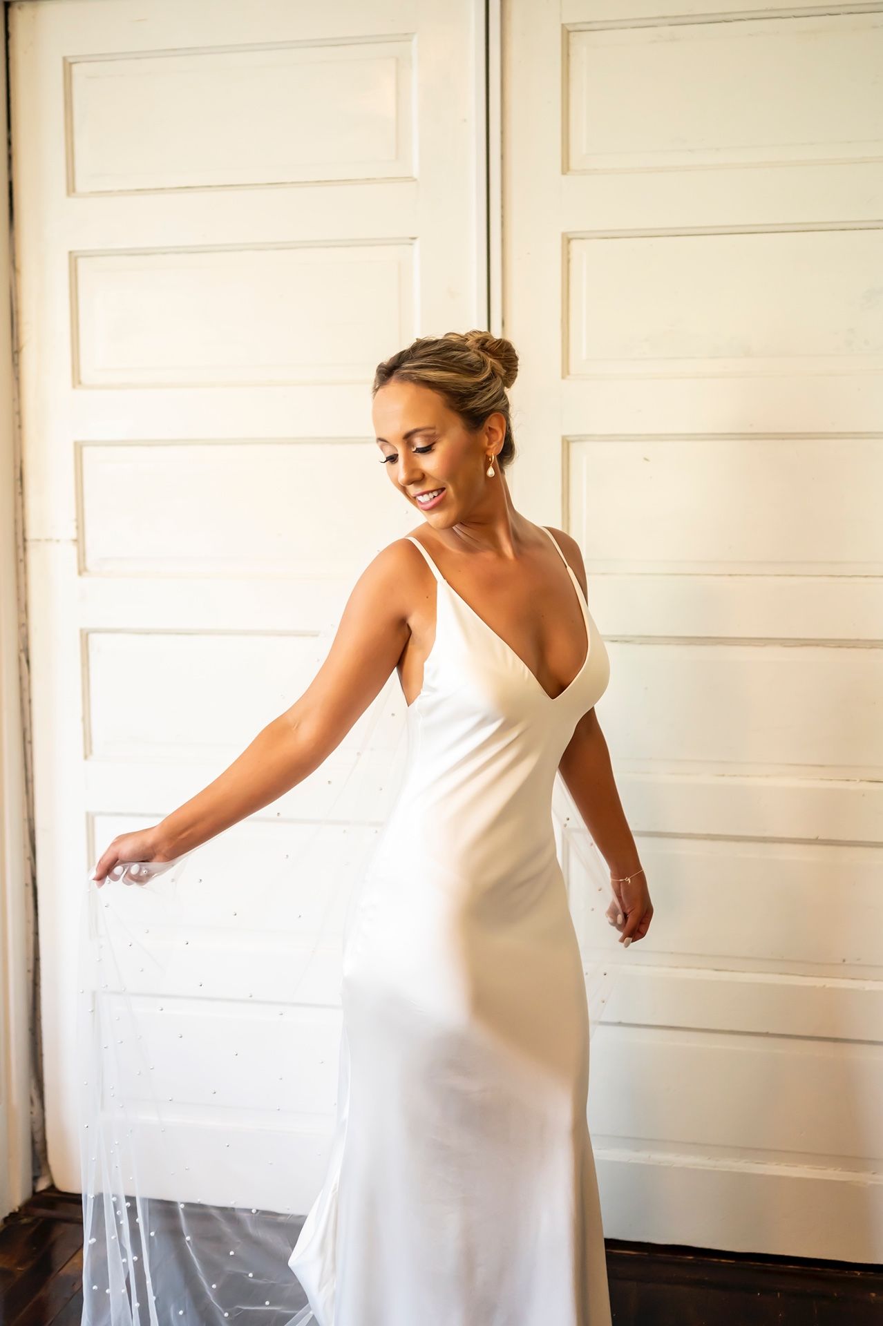 A bride in a classic white sleeveless gown gracefully twirls and dances in sequence against a white paneled wall.