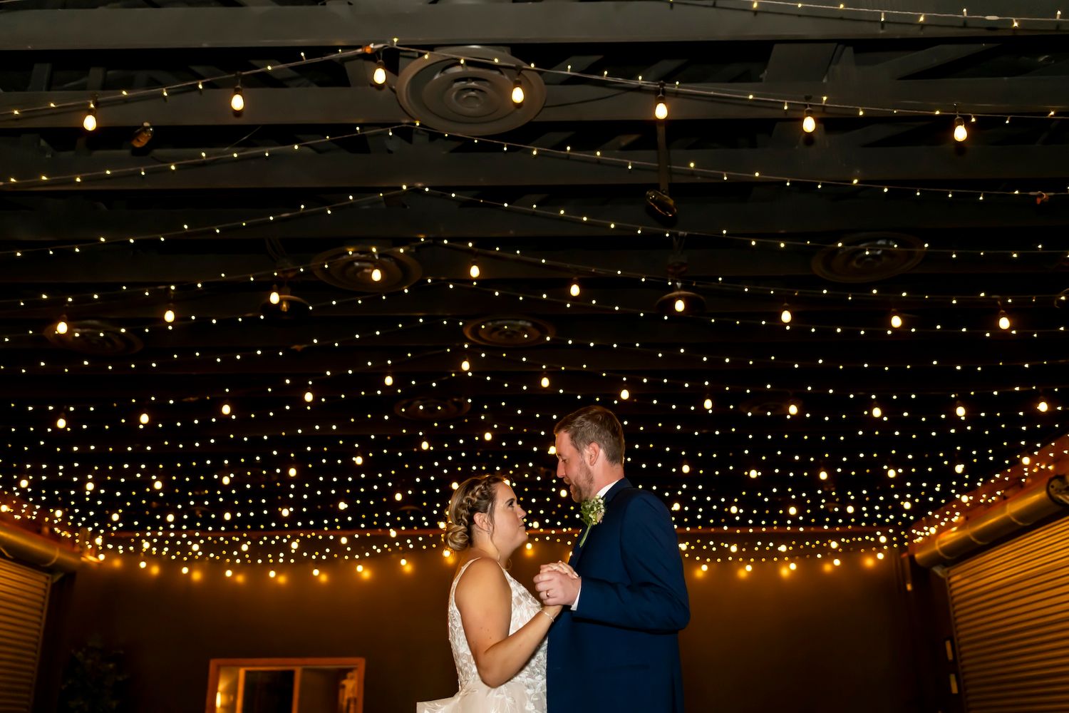 A couple shares their first dance under a magical canopy of string lights at their wedding reception.