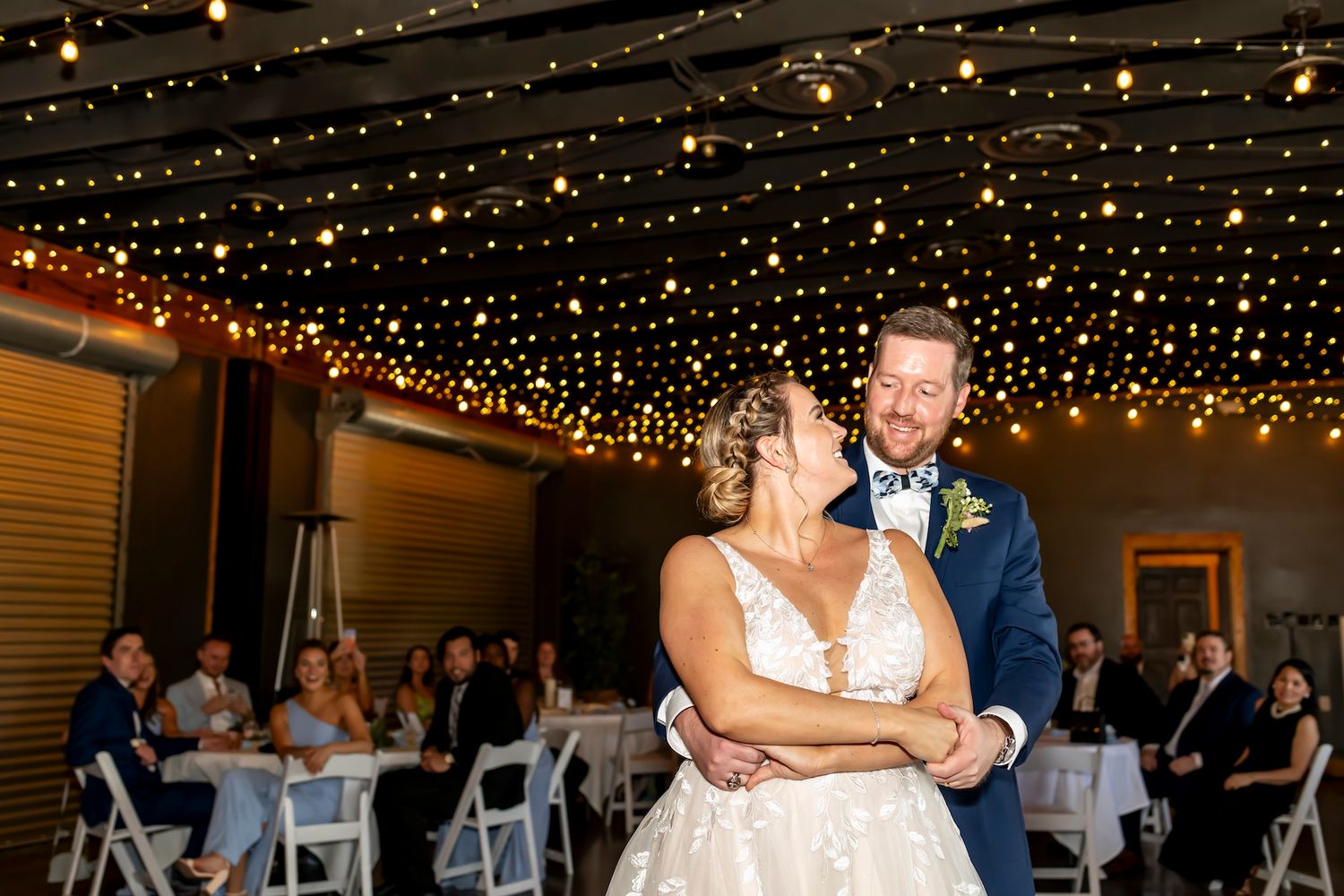 A couple dances and laughs together during their wedding reception beneath a magical canopy of string lights.