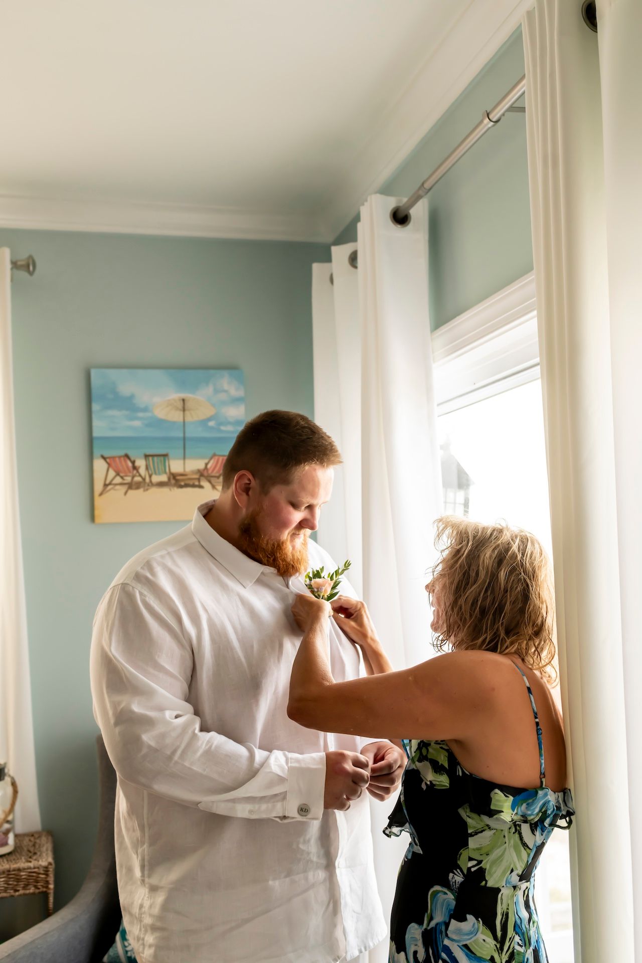 Two people getting ready for a formal event in a room with beach artwork and mint green walls.