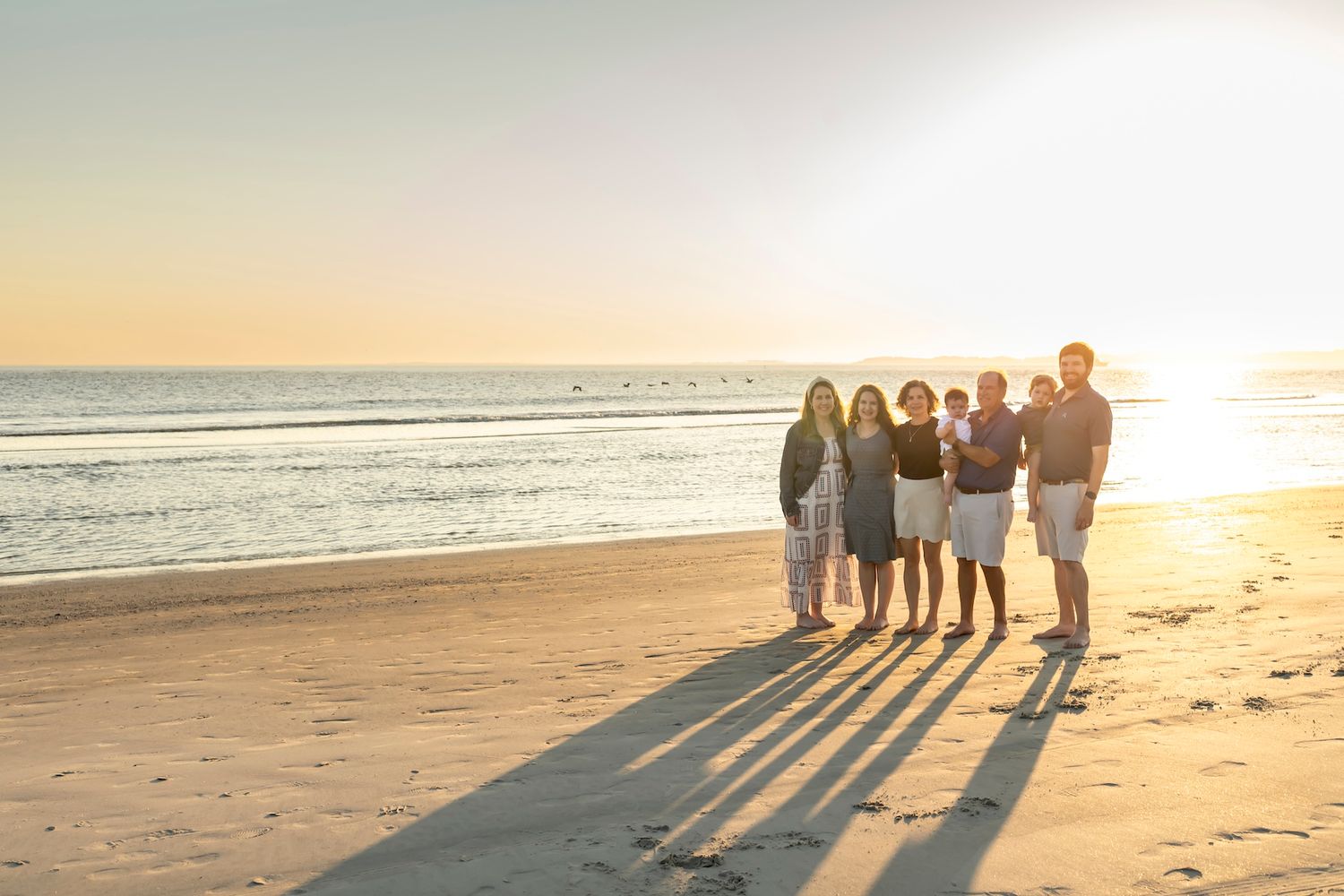 Silhouettes of people walking along a beach at sunset with long shadows cast on the sand.
