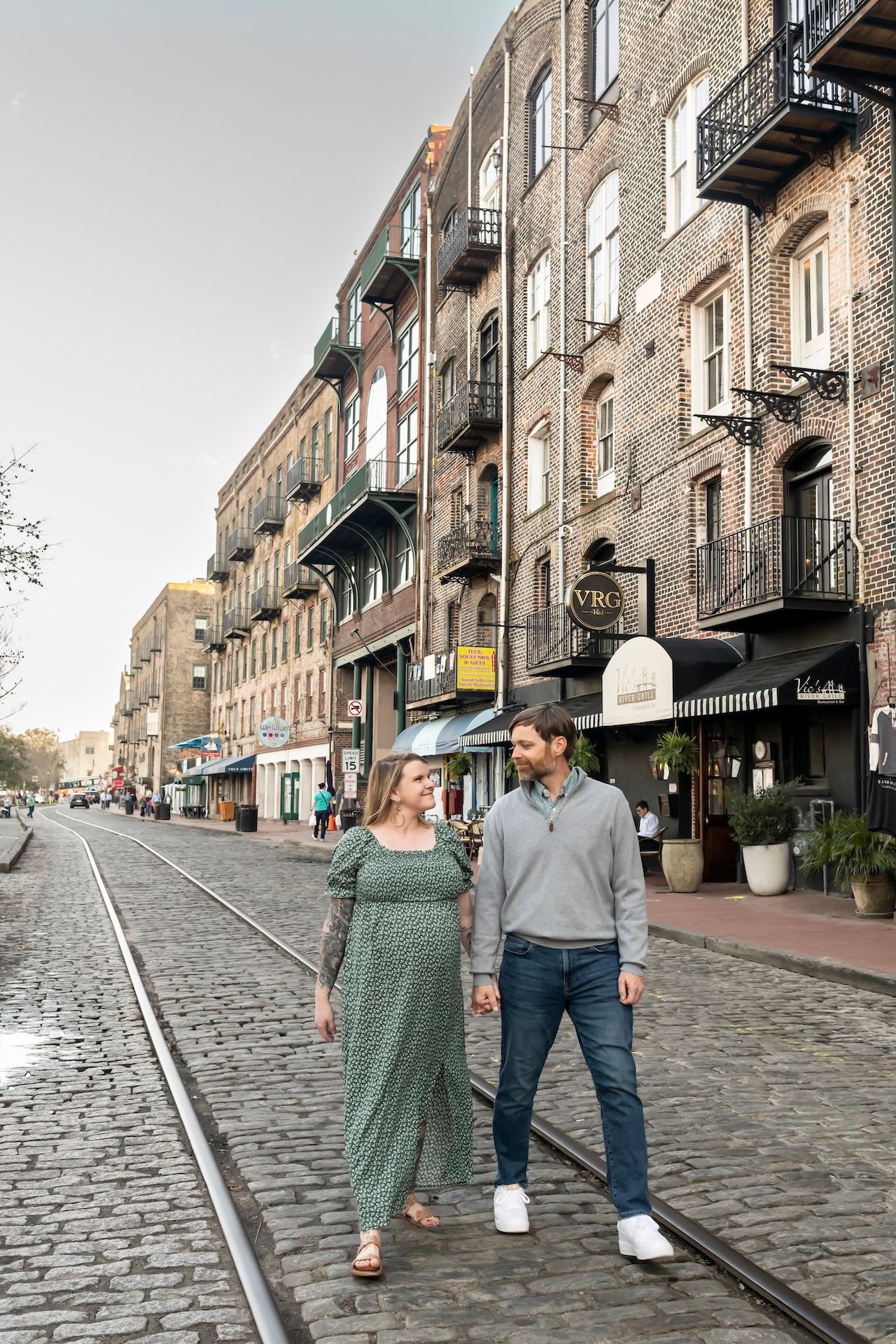 Couple walking along cobblestone street with historic brick buildings and shops on River Street in Savannah, Georgia.