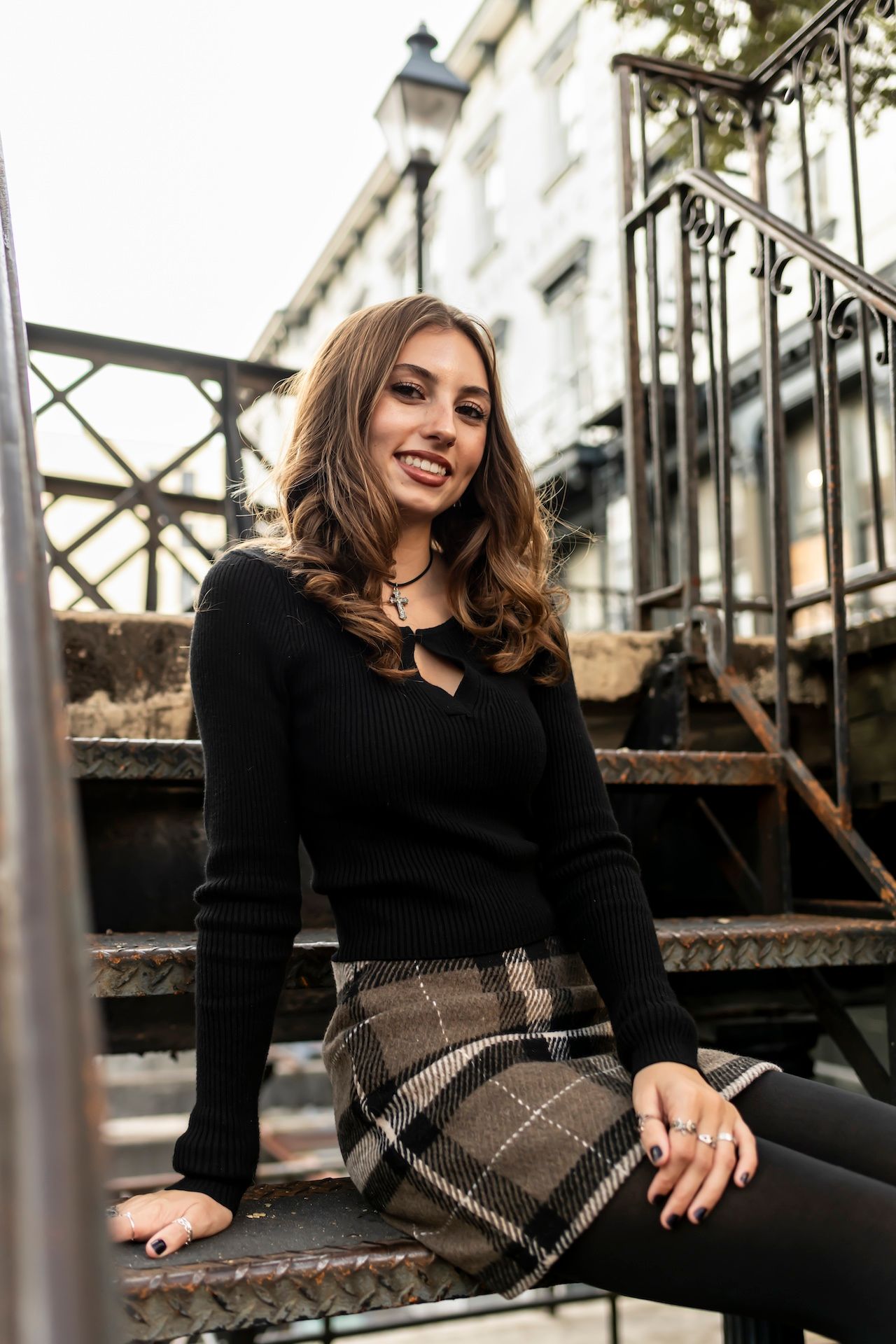 Young woman in black sweater and plaid skirt lounging on outdoor steps on an autumn day.