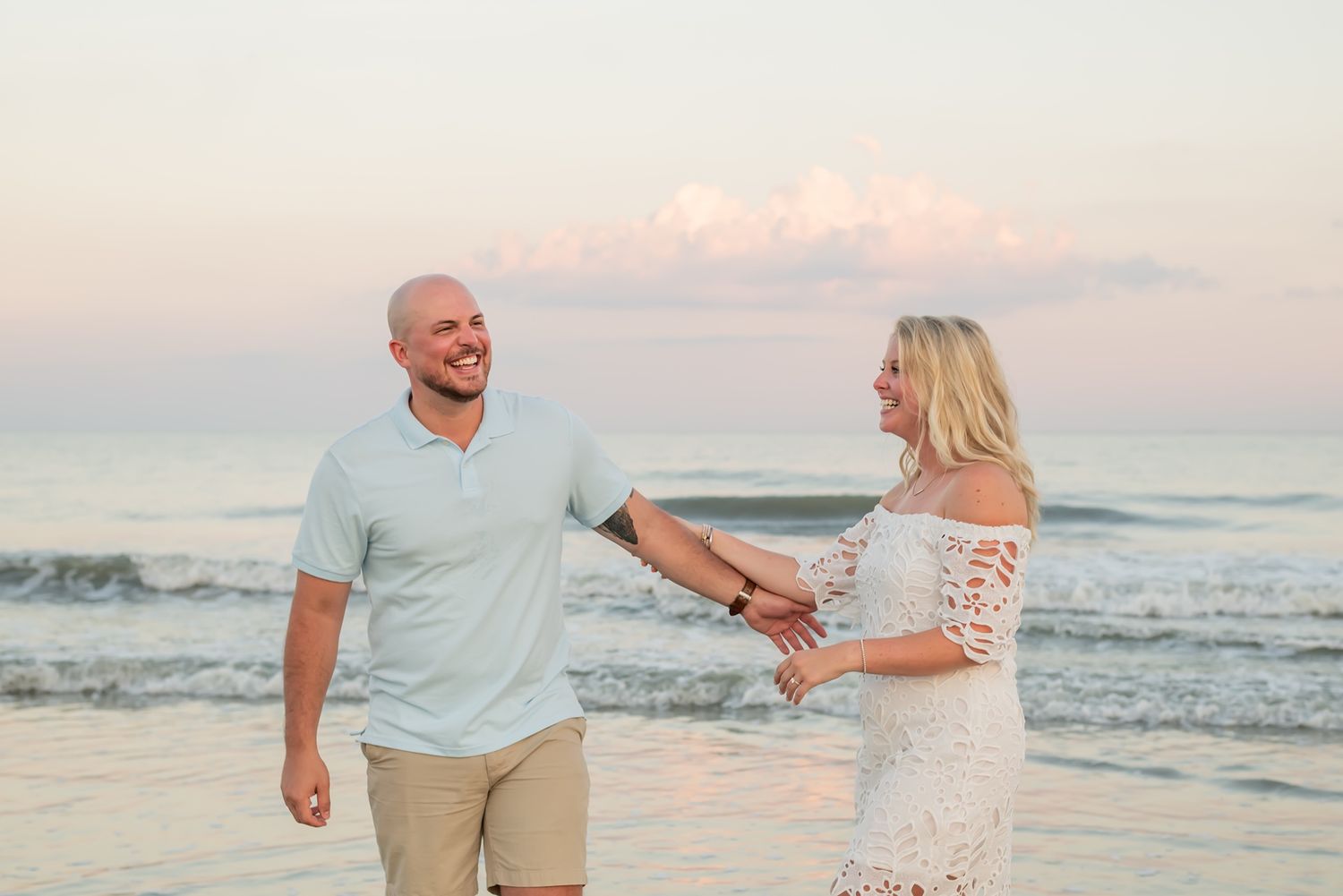 Couple walking hand in hand along a beautiful beach at sunset with ocean waves crashing in the background.