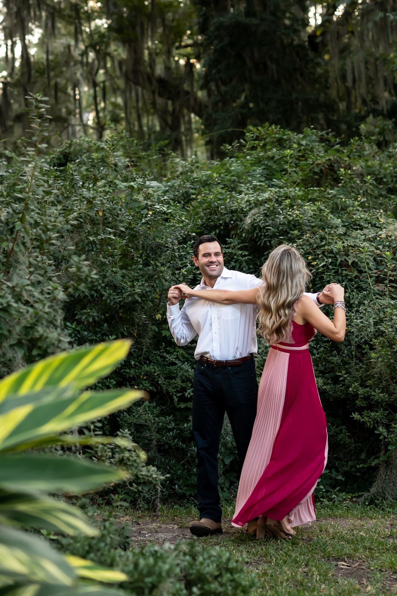 Dancing together joyfully amidst natural greenery and Spanish moss in a garden setting.